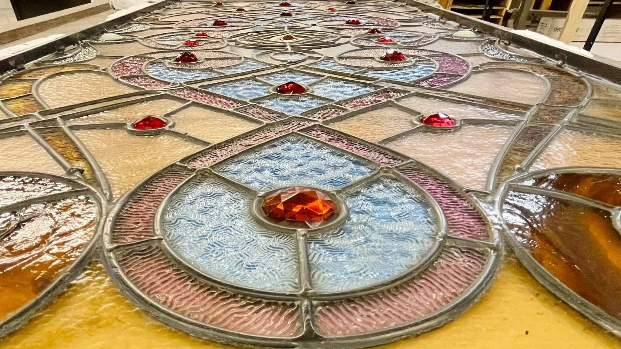 Close-up of a stained glass window with intricate patterns, colorful glass pieces, and red gem-like accents.