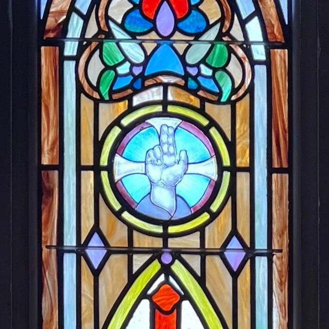 Stained glass window showing a hand making a peace sign with two fingers raised.