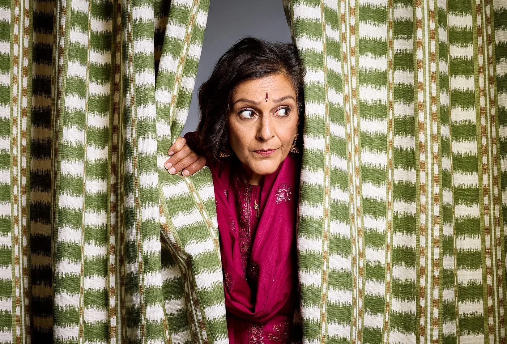 Meera Syal peering through some curtains. Photographed by Amy Brammall