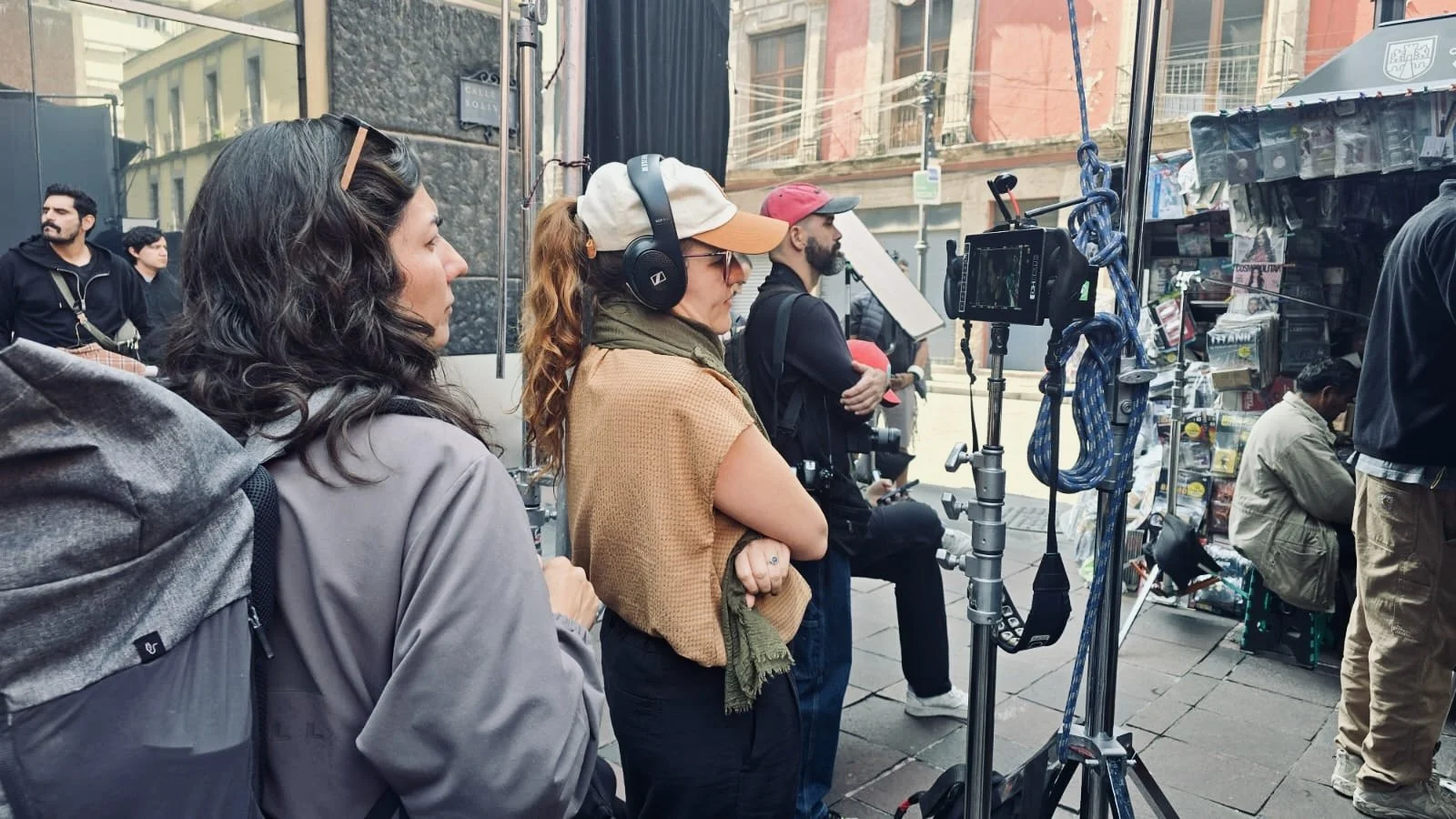 People filming a street scene near a newsstand with cameras and equipment