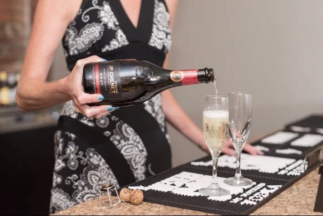 A woman in a black and white patterned dress pouring champagne into a flute. Mobile bar service. Champagne toast.