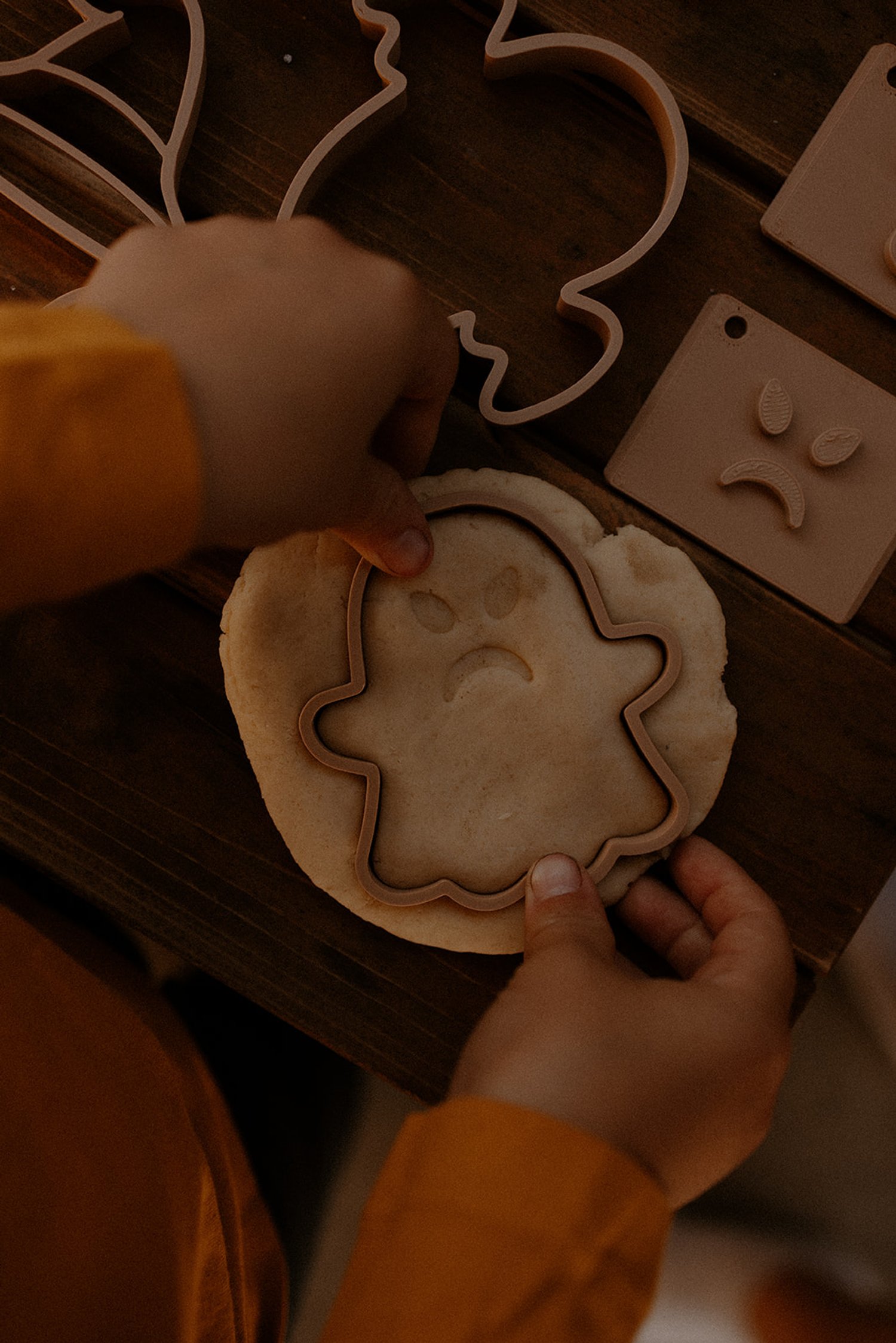 Ghost-shaped playdough cutter and stamp set with spooky face impressions on wooden background
