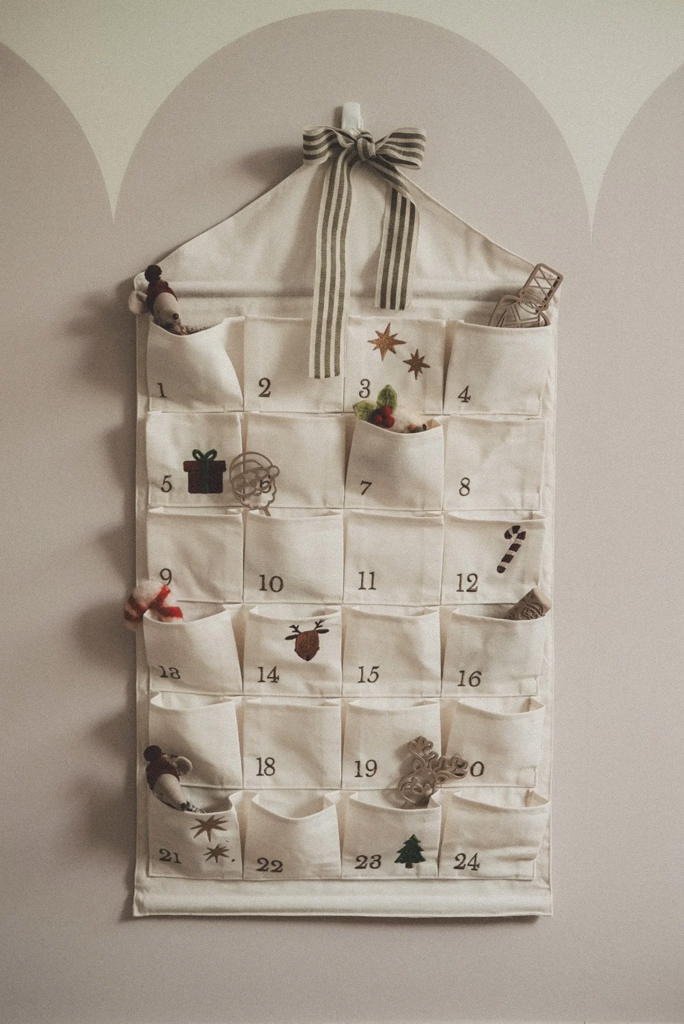 Linen hanging advent calendar with numbered pockets displayed beside a decorated Christmas tree