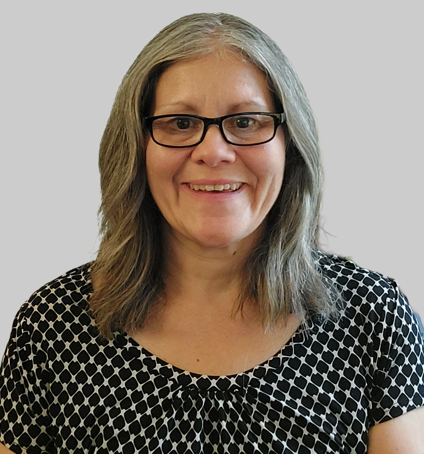 A woman with shoulder-length gray hair, wearing glasses and a black and white patterned top, smiling at the camera.