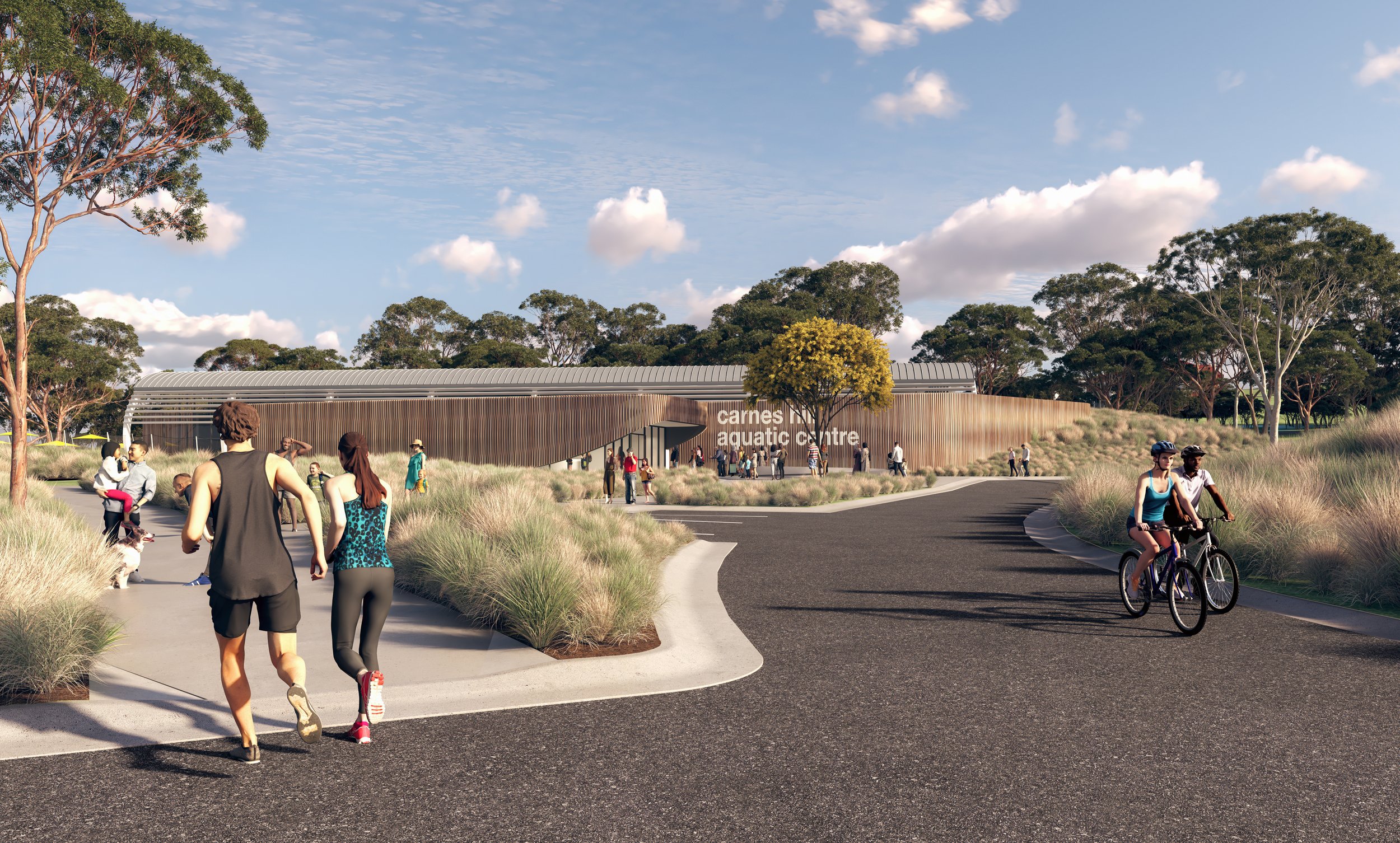 People walking and cycling towards the Carnes Hill Aquatic Centre, a modern building with a curved wooden exterior, surrounded by trees and landscaping, on a sunny day with a partly cloudy sky.