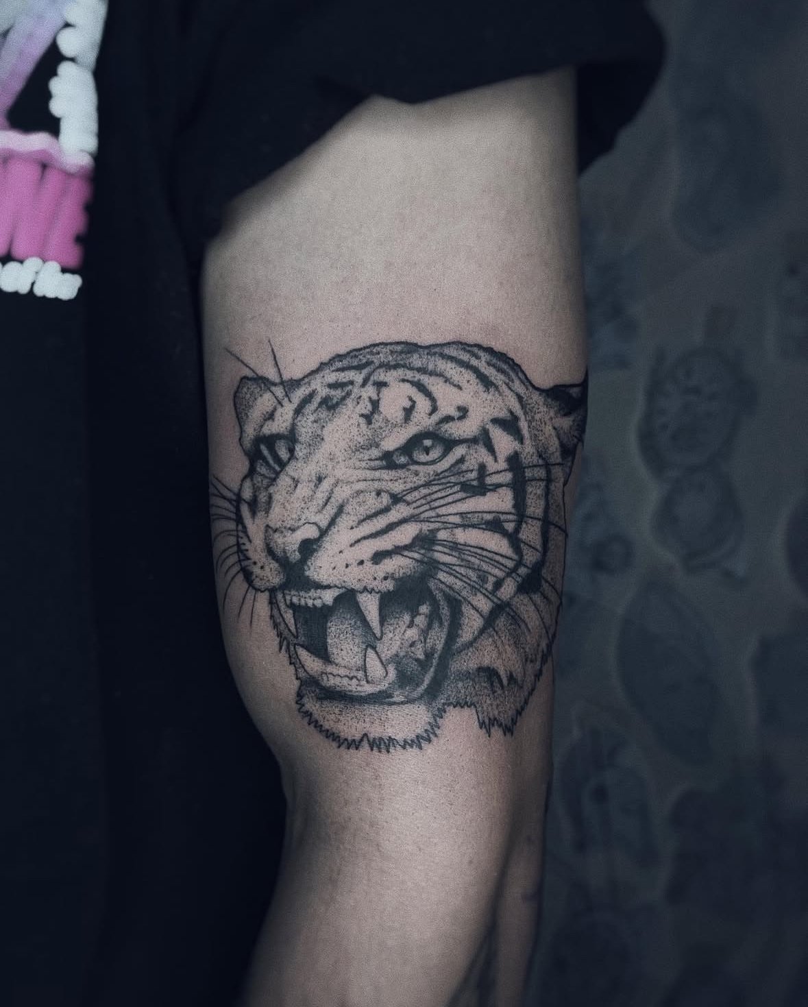 A tiger tattoo with a defensive expression, placed on the outer bicep and created exclusively using black ink By Davila