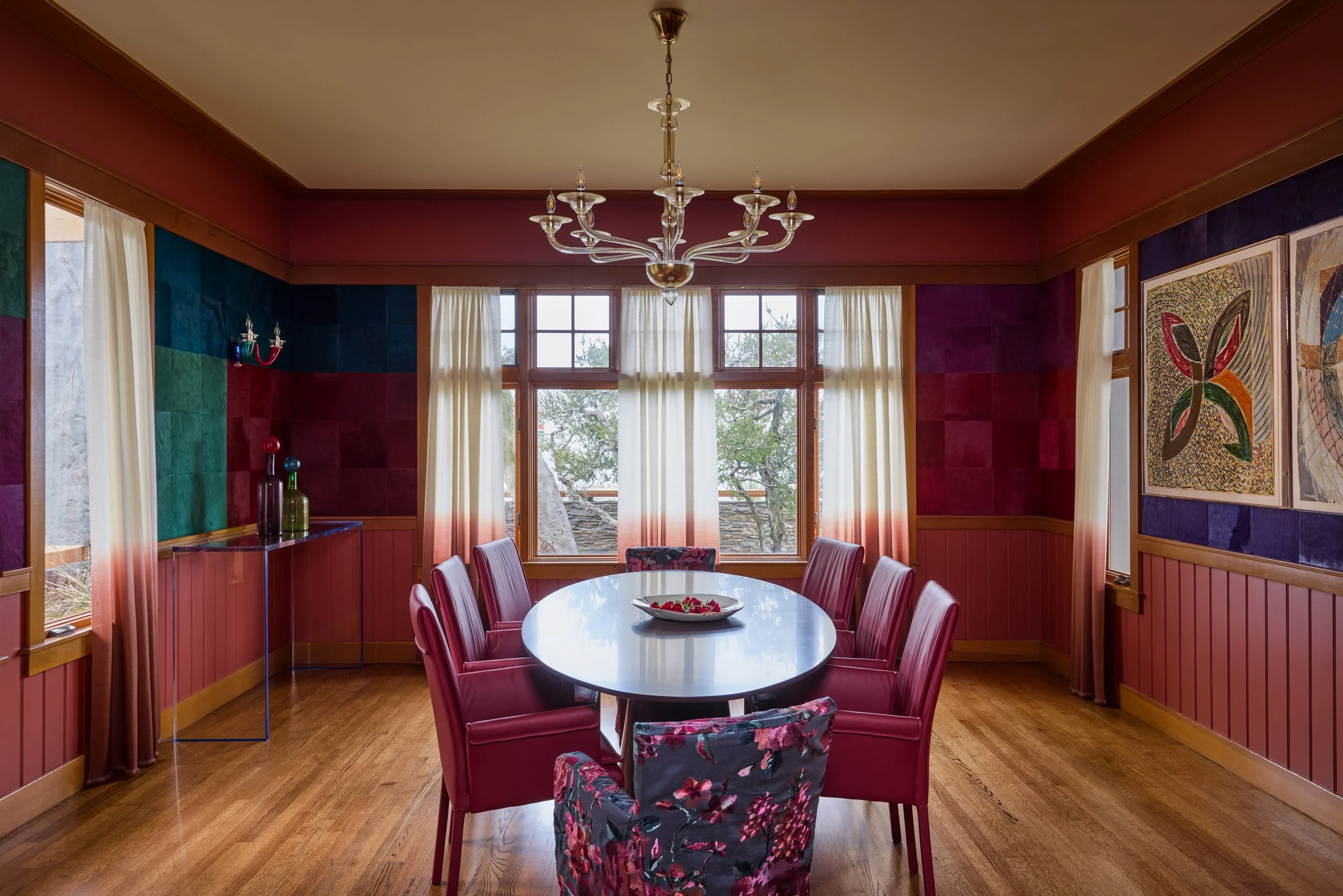 This vibrant and artfully curated dining room makes a bold design statement with its rich color palette and modern eclectic style. The walls are adorned with a patchwork of velvet-textured panels in jewel tones—ranging from emerald green to deep plum
