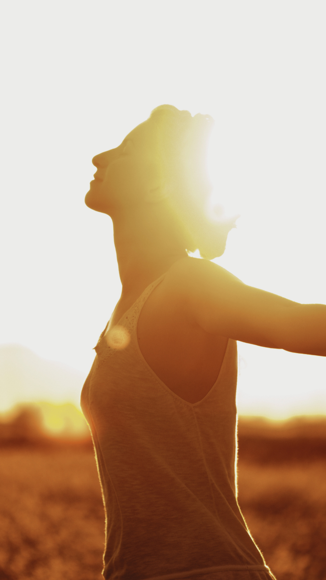 A woman is standing outdoors during sunset with her arms raised, enjoying the sunlight shining behind her in a natural setting. Bend Thoughts & Therapy in Bend, OR.