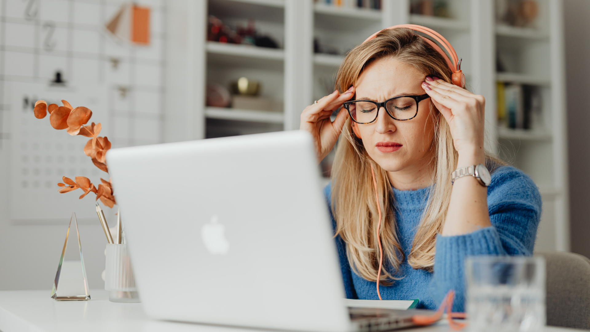 Woman with glasses and headphones holding her head in frustration at a desk with a laptop. Bend Thoughts & Therapy in Bend, OR.