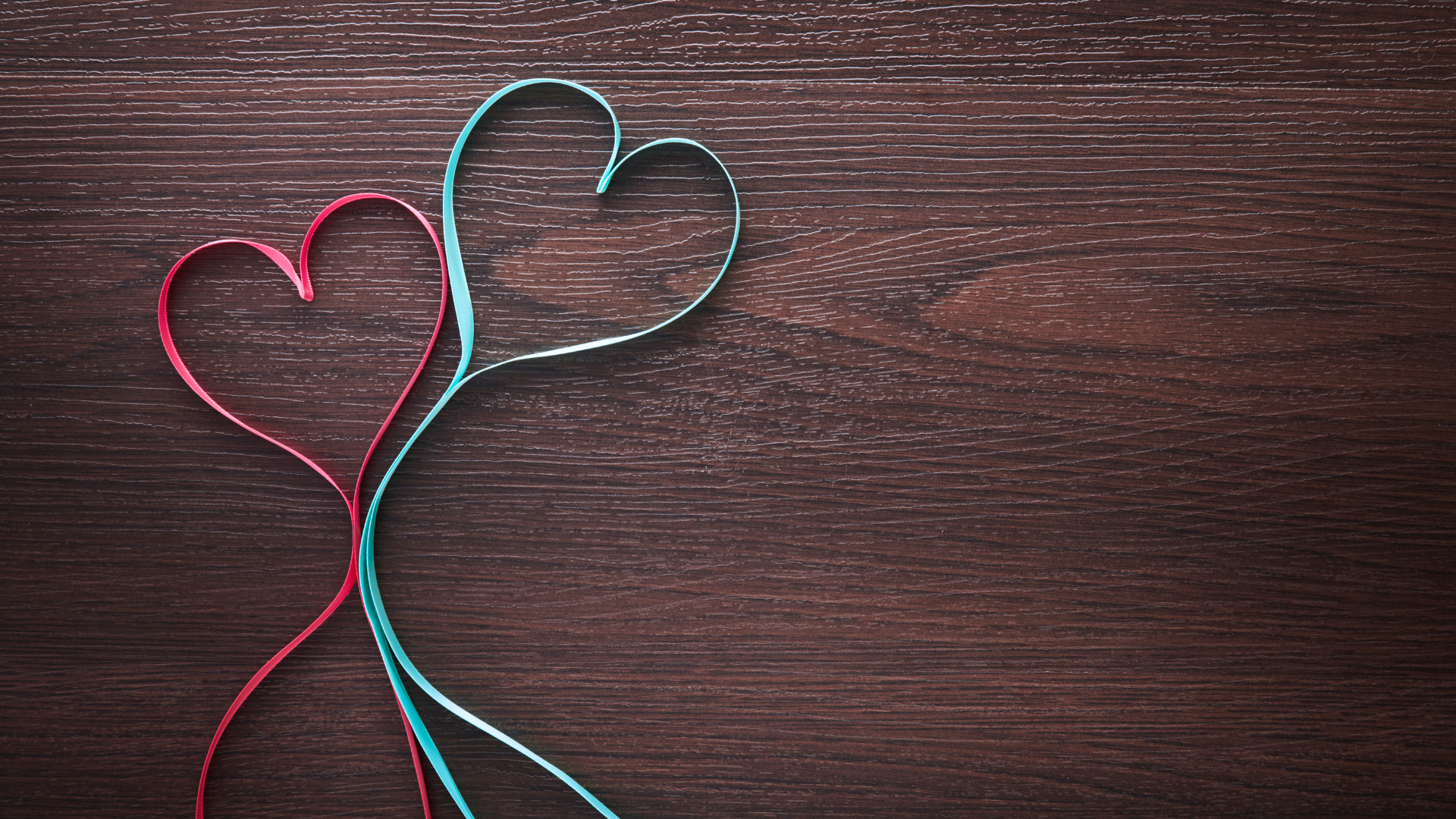 Two wire heart shapes, one pink and one light blue, placed on a dark wooden surface. Affordable therapy in Bend, OR.