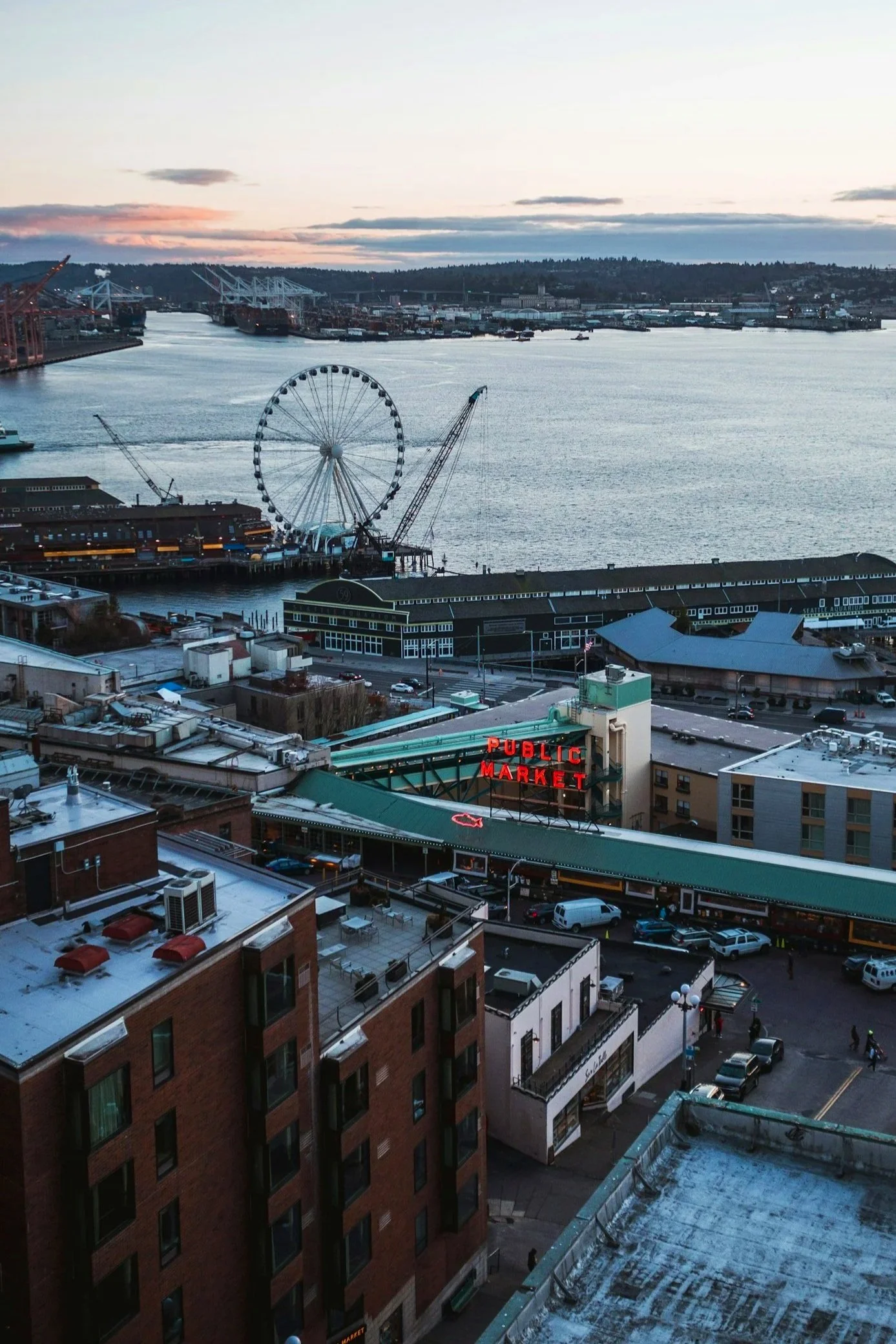 The Seattle waterfront at sunset overlooking Pike's Place Public Market, including the famous neon sign. In the distance is the Seattle Greet Wheel.