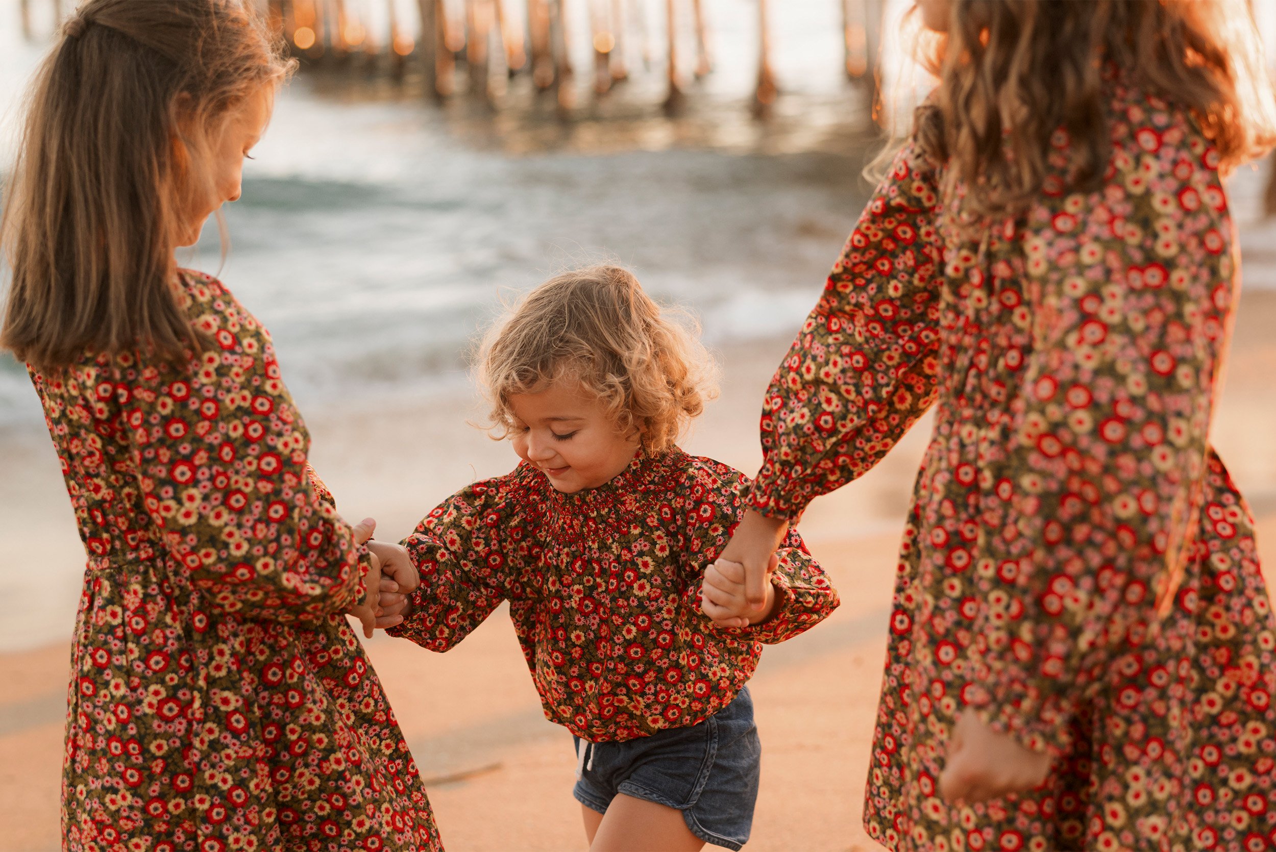 Highly recommended family photographer captures sisters in matching floral dresses on beach