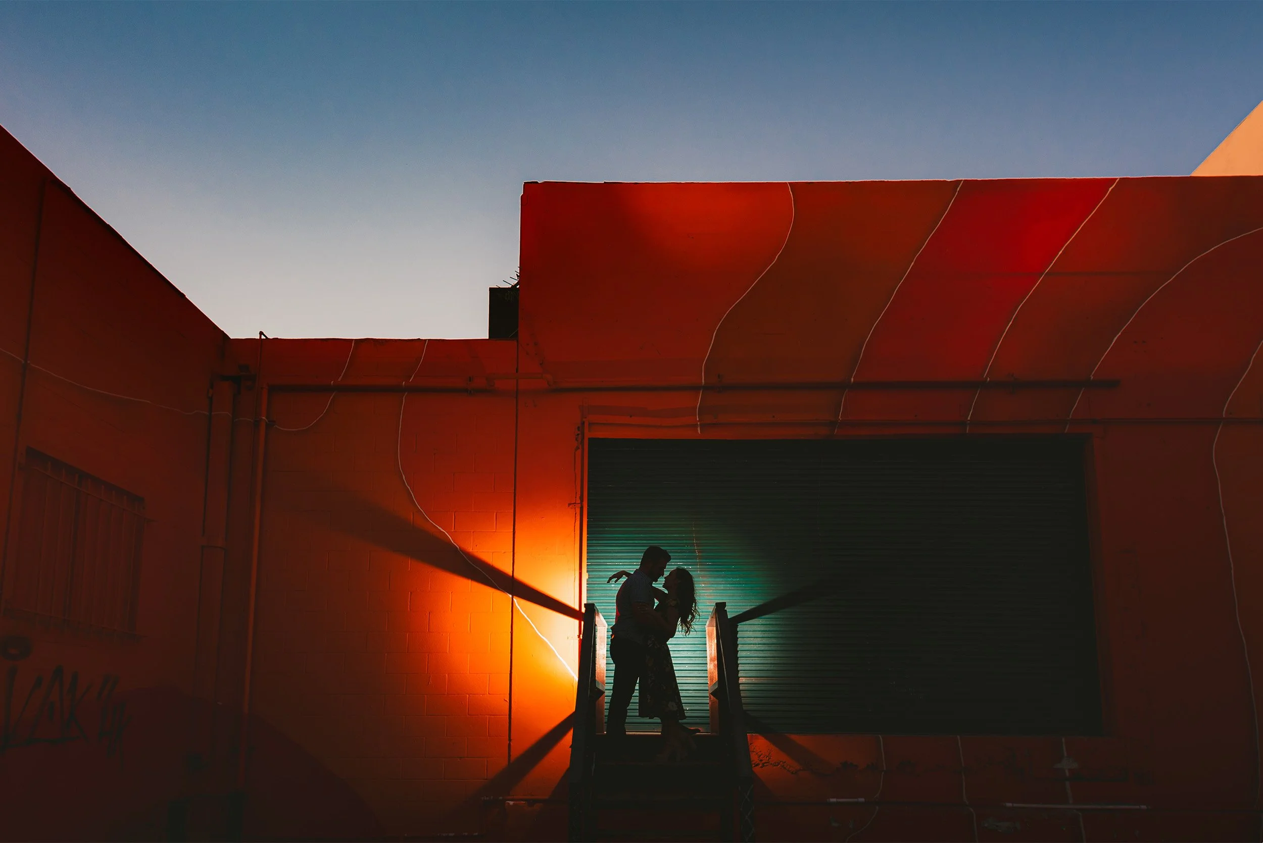 Silhouette of couple embracing on a staircase against a colorful sunset wall mural,  Los Angeles engagement photography