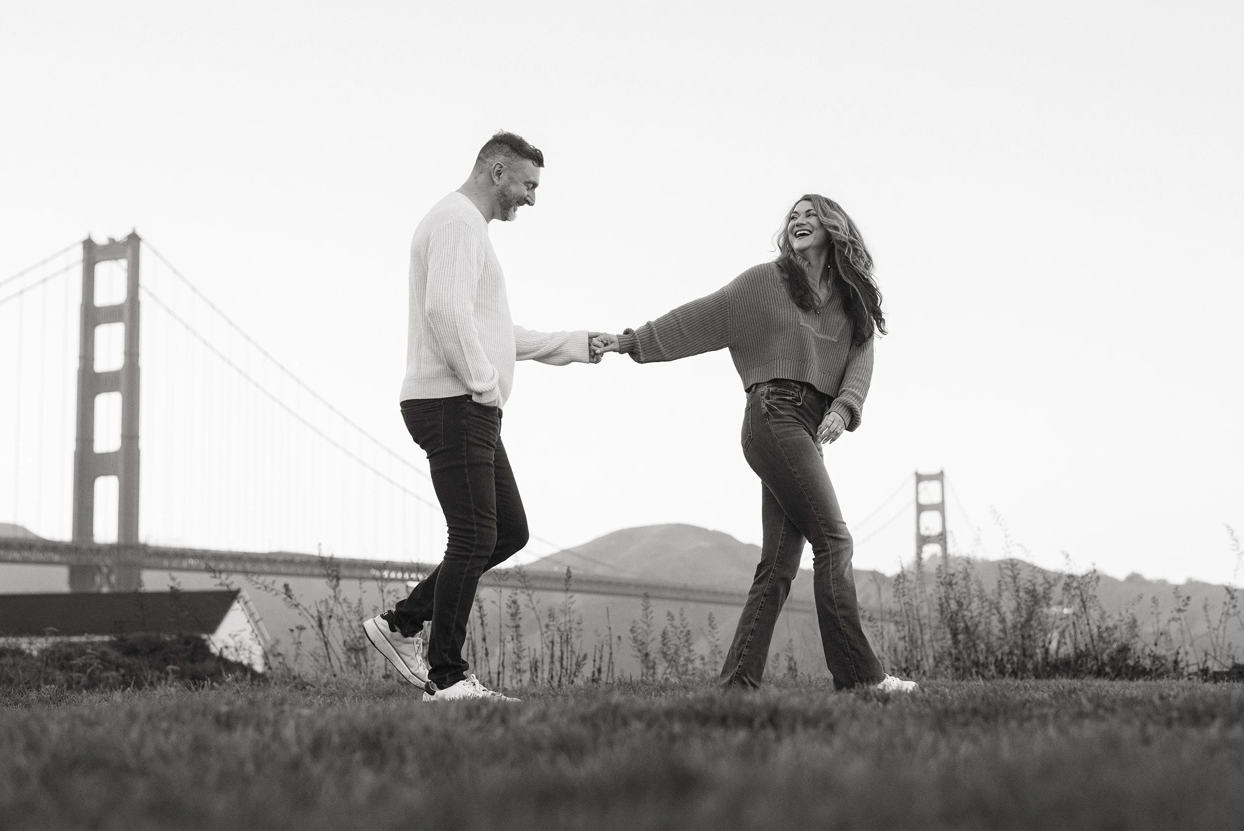 Award-winning engagement photographer from Orange County captures couple laughing hand in hand with the Golden Gate Bridge in San Francisco behind them
