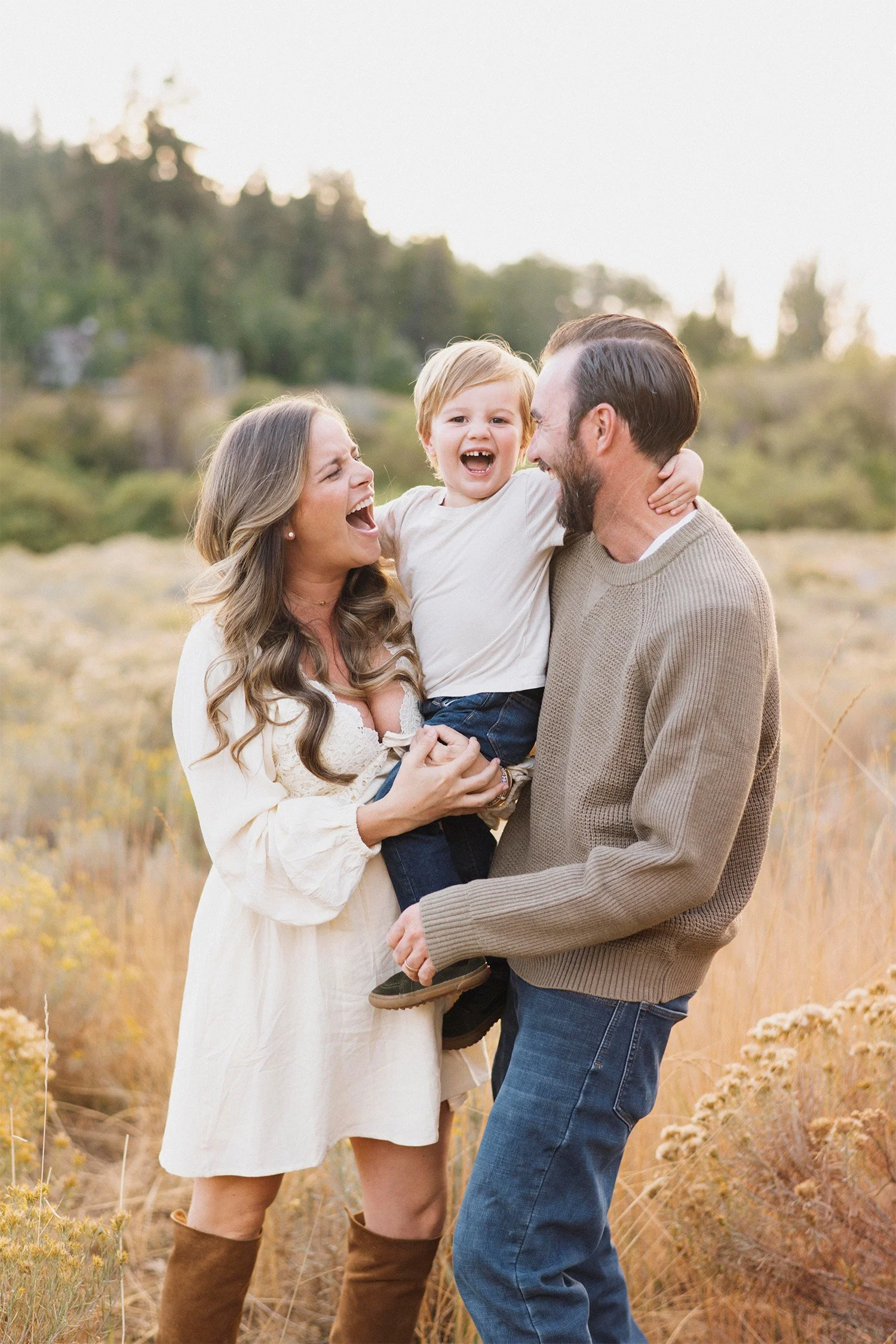 Award-winning family photographer in Orange County captures pregnant mother and father laughing with their son in a golden field