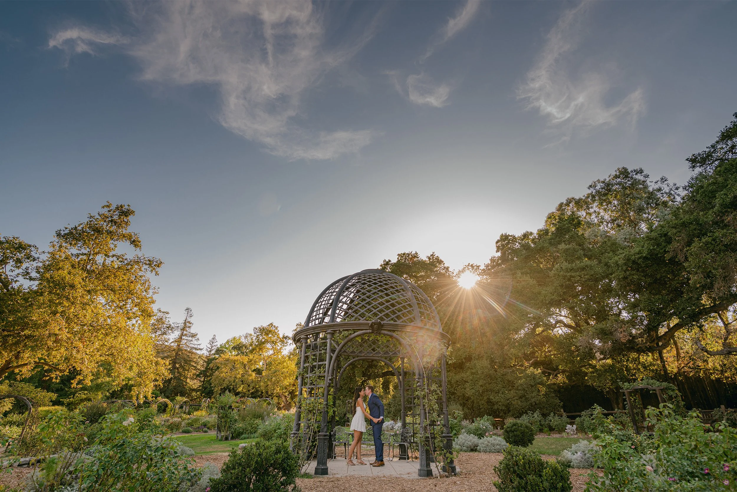 Couple kissing under iron gazebo in rose garden at golden hour, Orange County engagement photographer