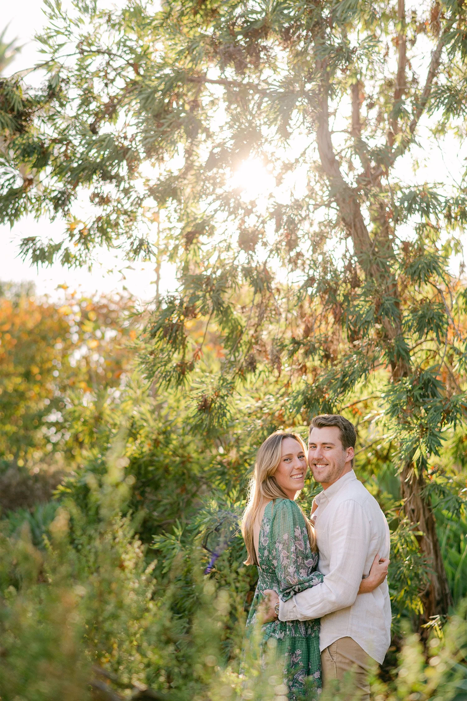 Orange County engagement photographer captures smiling couple beneath sunlit trees in lush greenery