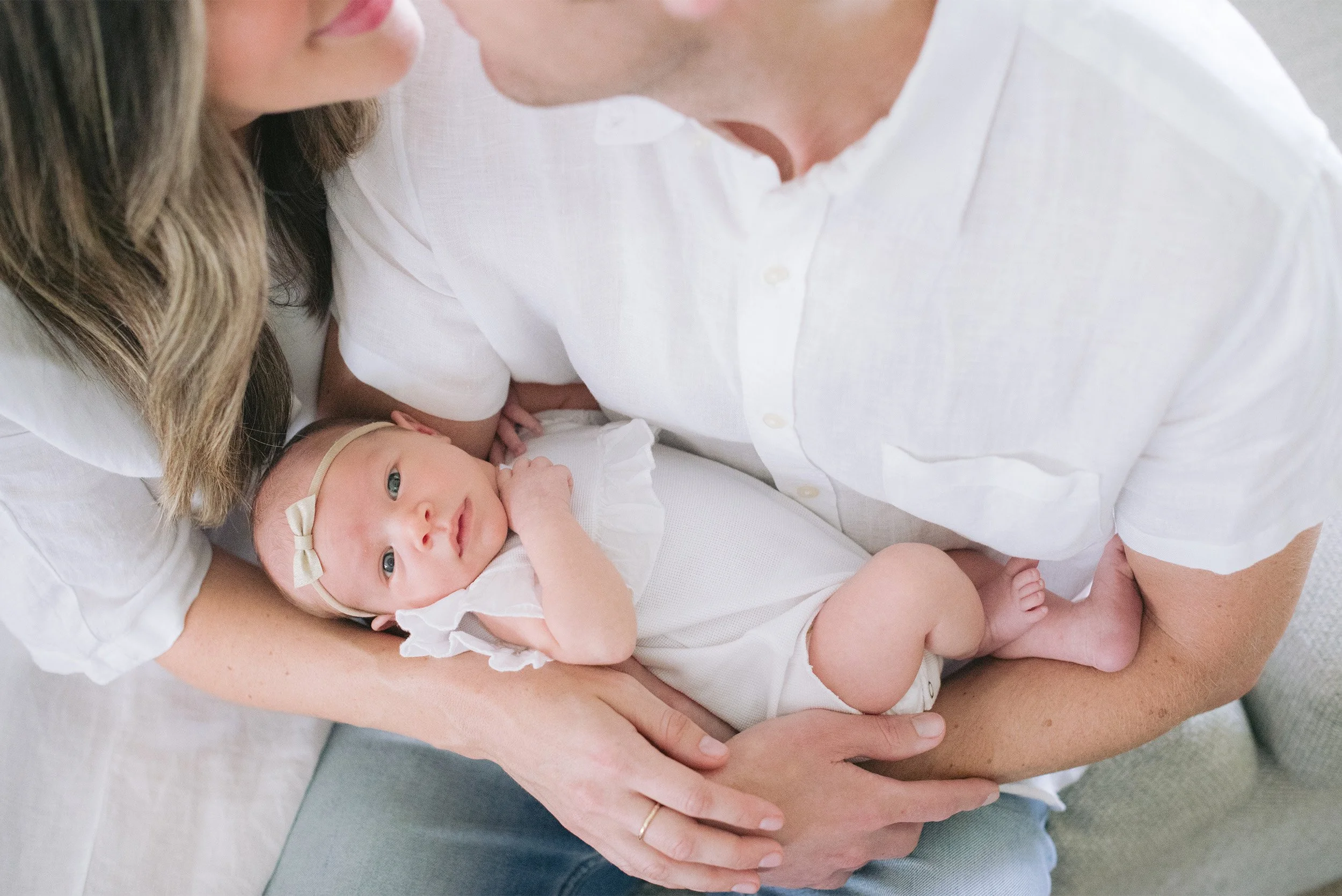Orange County baby photographer captures overhead portrait of parents holding baby girl with bow headband