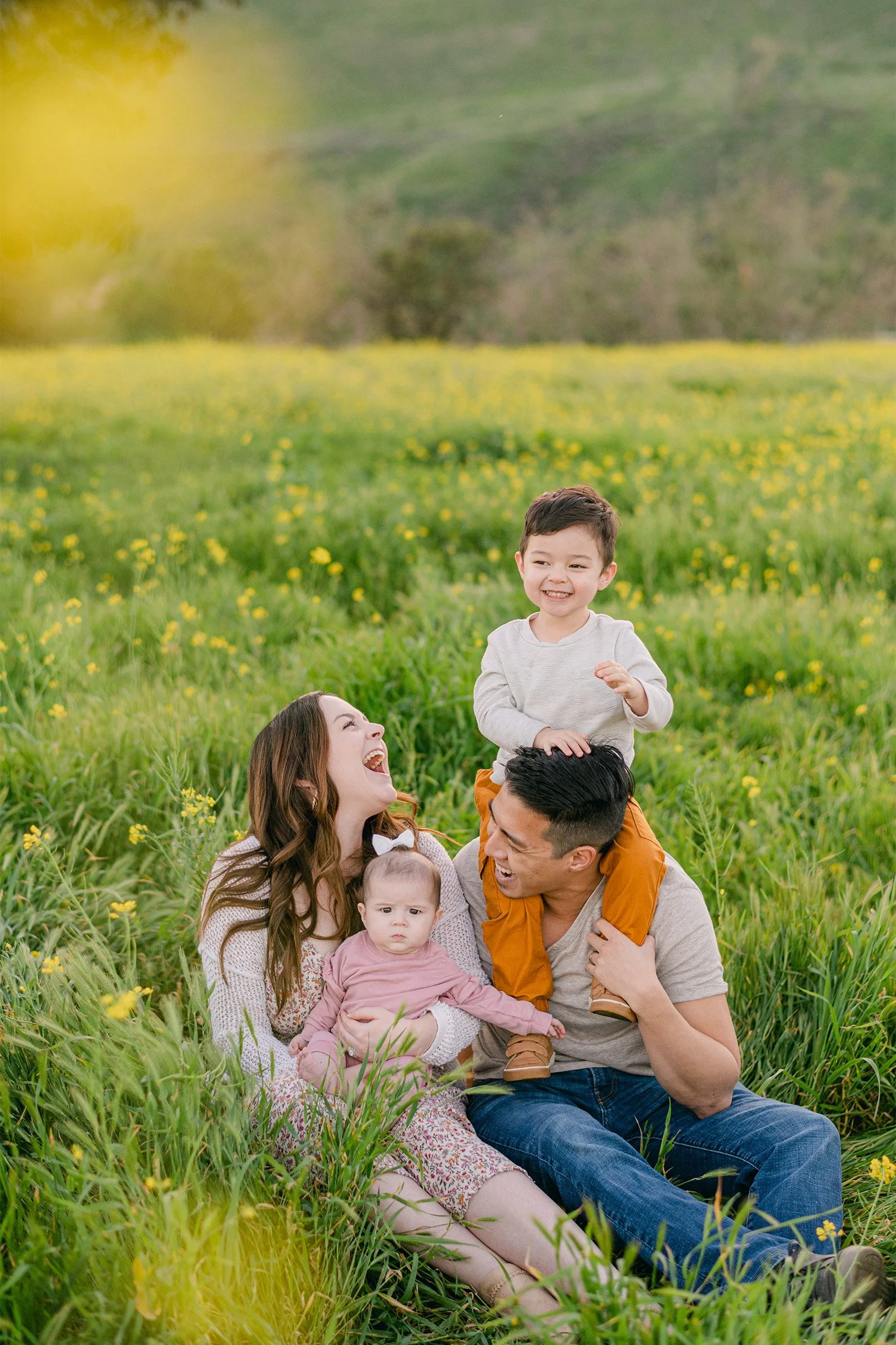 Highly recommended family photographer captures laughing family of four sitting together in a wildflower field, Orange County family photoshoot locations