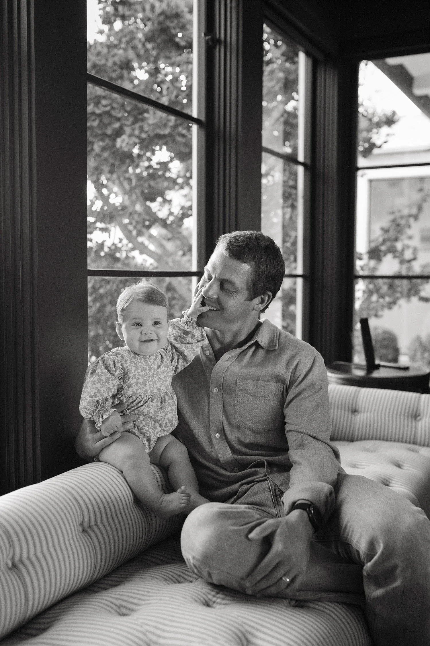 Highly recommended family photographer in Orange County captures father and baby daughter sharing a laugh by a window seat