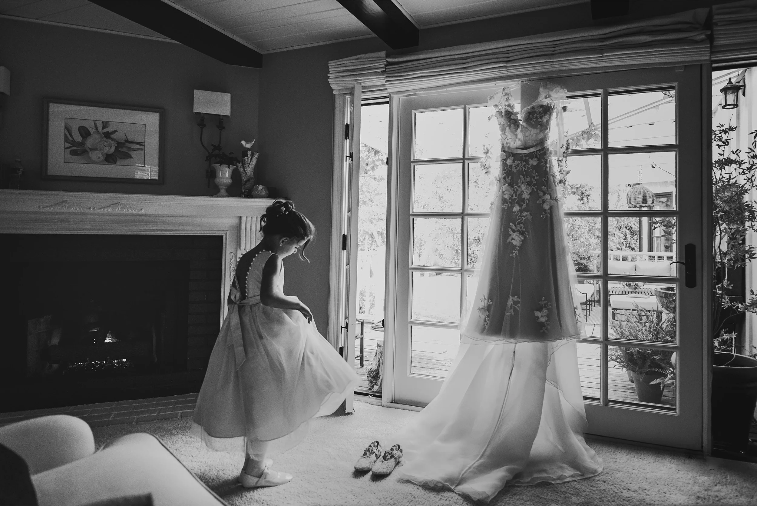 Flower girl twirling her dress beside hanging wedding gown, black and white getting-ready photo