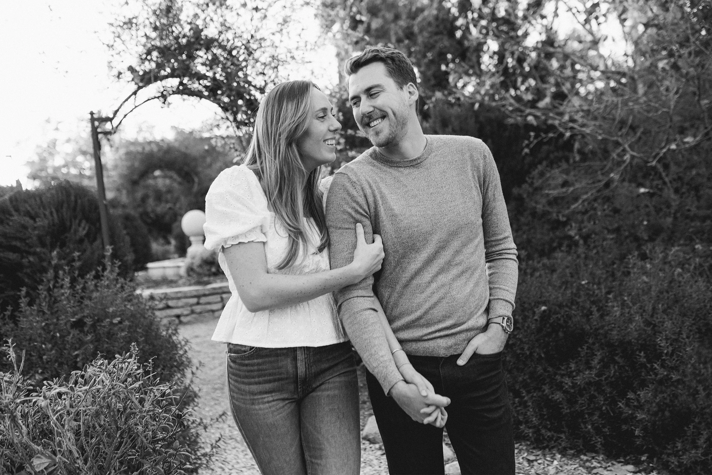 Couple laughing together arm in arm on garden pathway, award-winning engagement photographer