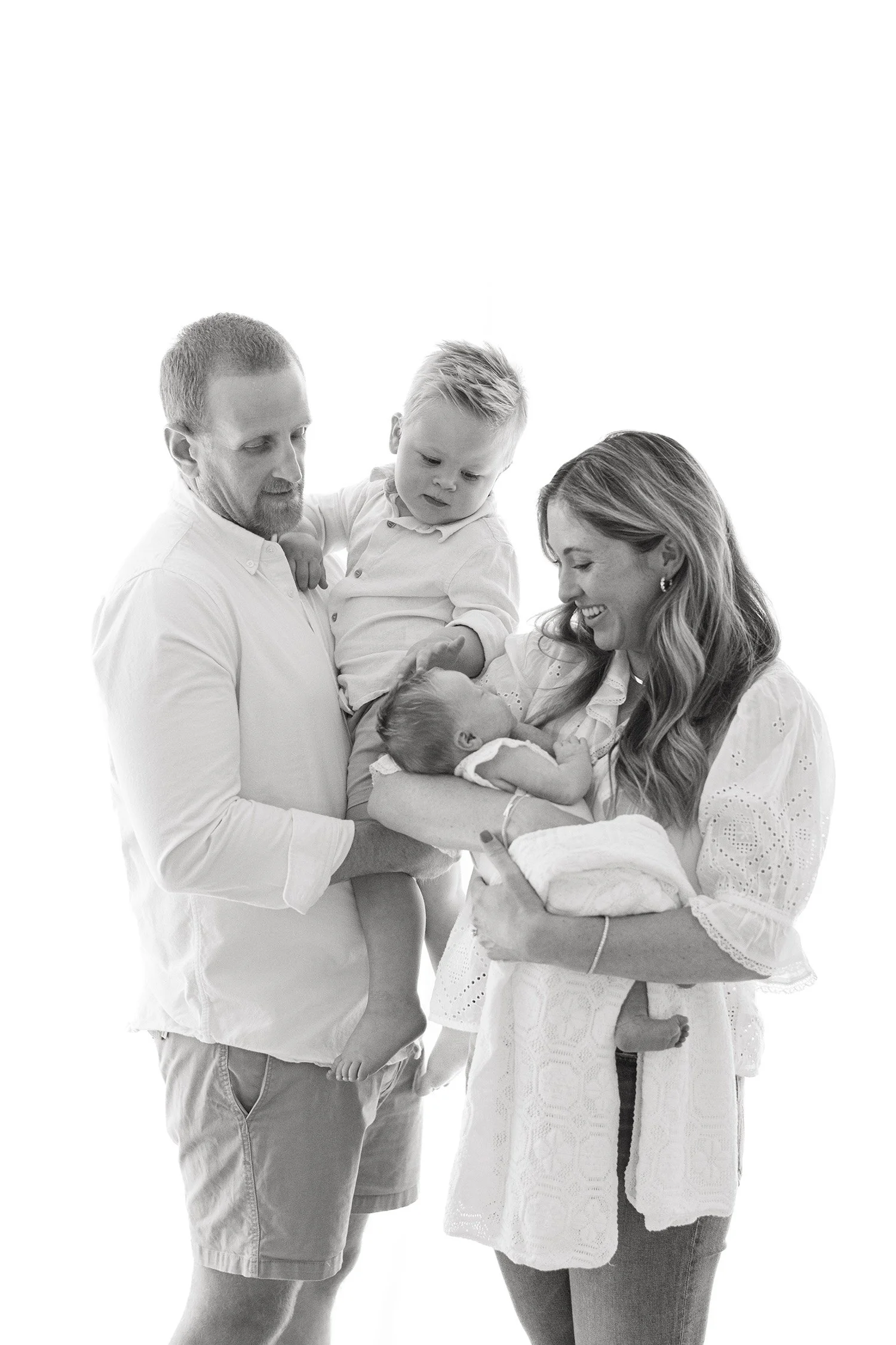 Black and white family portrait with toddler and newborn on white backdrop, award-winning baby photographer located in Orange County