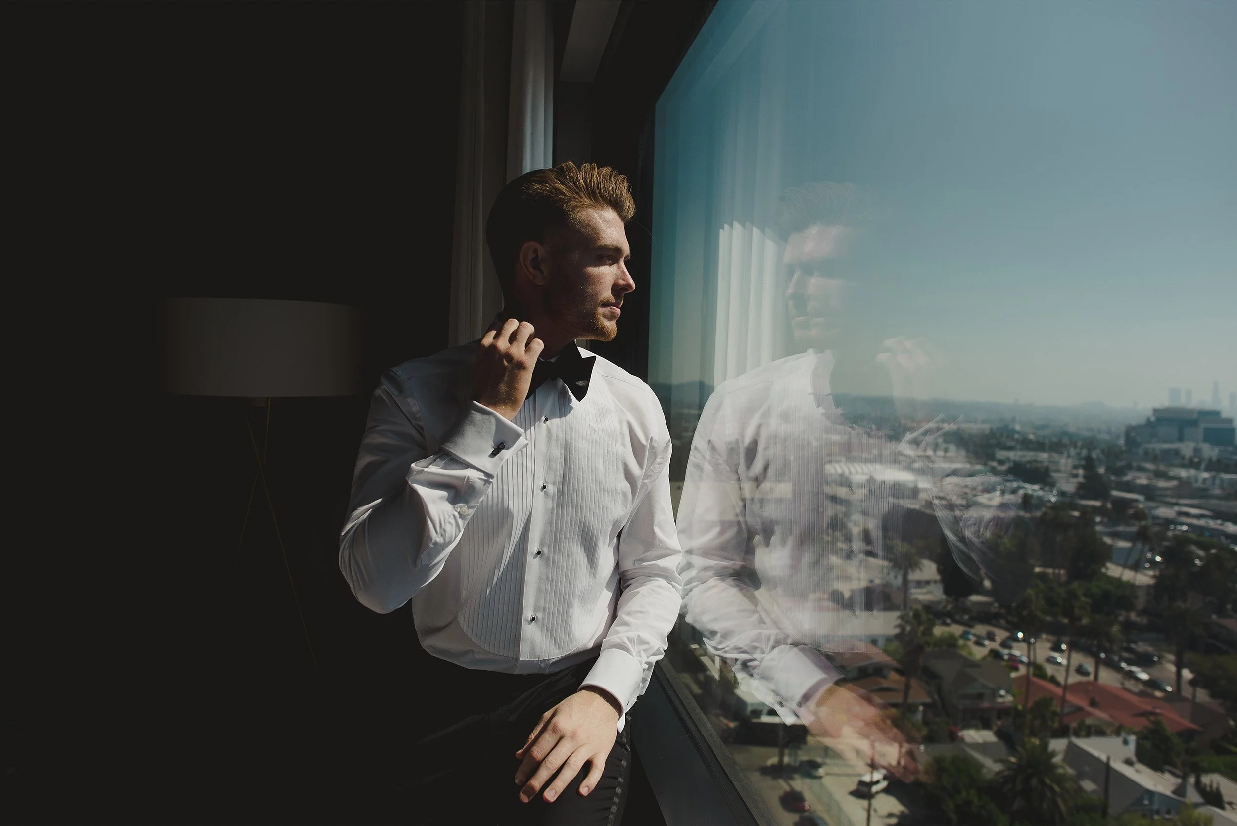 Highly recommended wedding photographer in Los Angeles captures groom's contemplative reflection in floor-to-ceiling window overlooking city