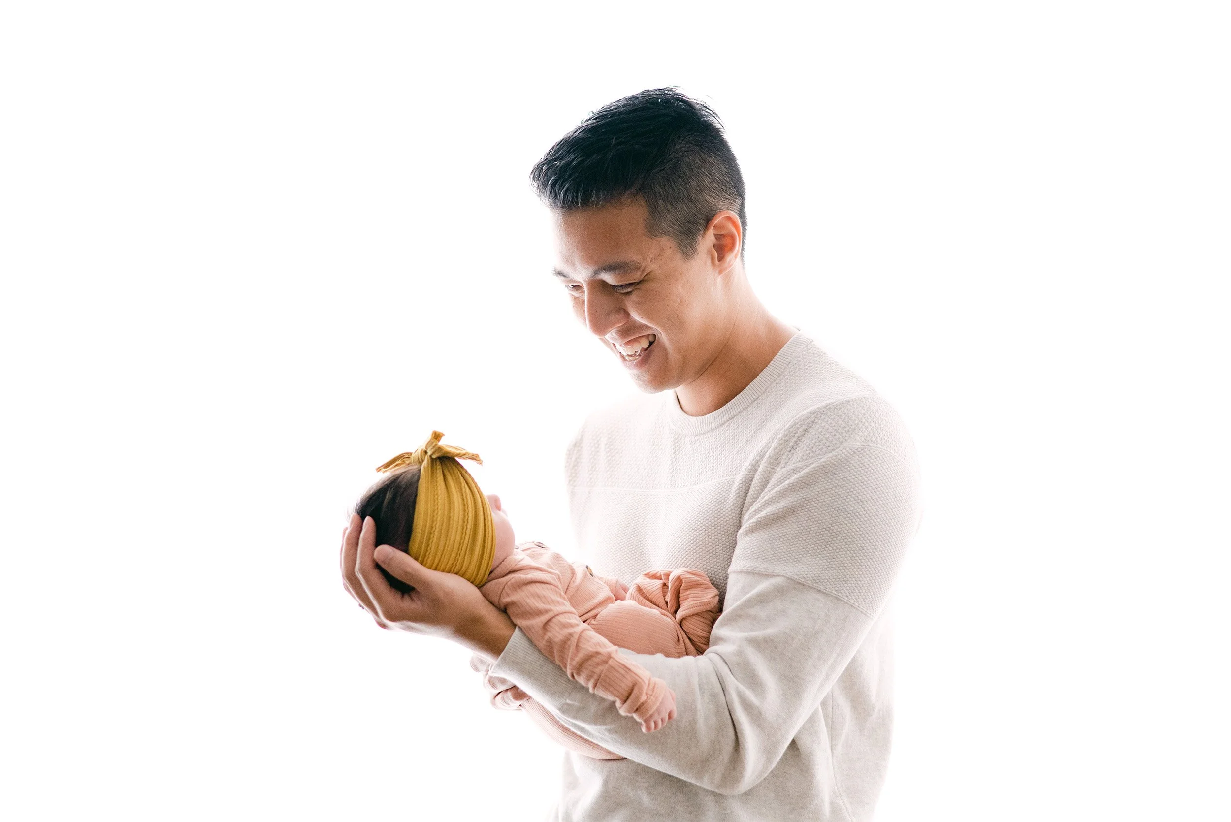 Proud father smiling down at newborn daughter in mustard headband, highly recommended baby photographer Orange County