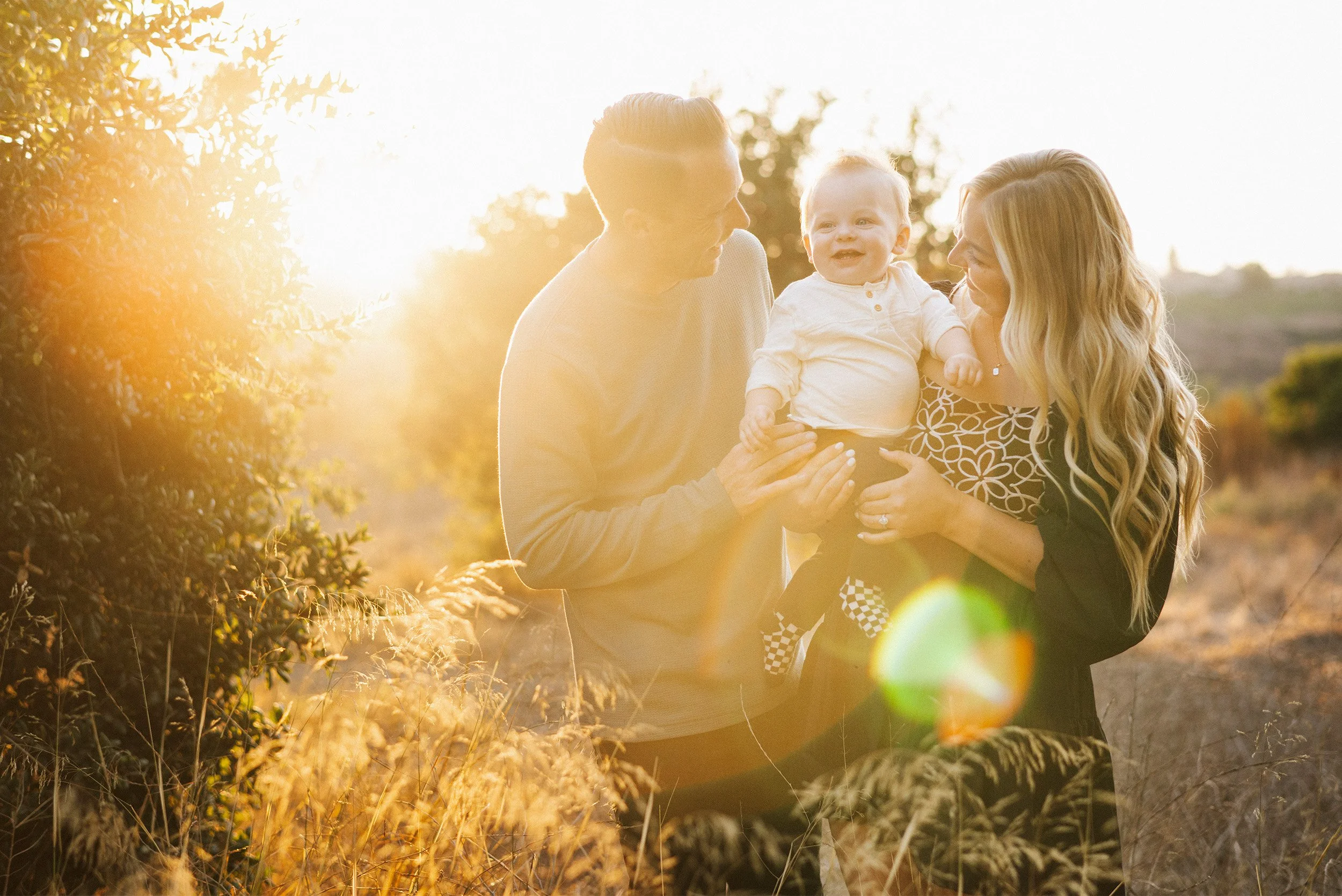 Award-winning family photographer in Orange County captures parents playing with laughing baby in golden light