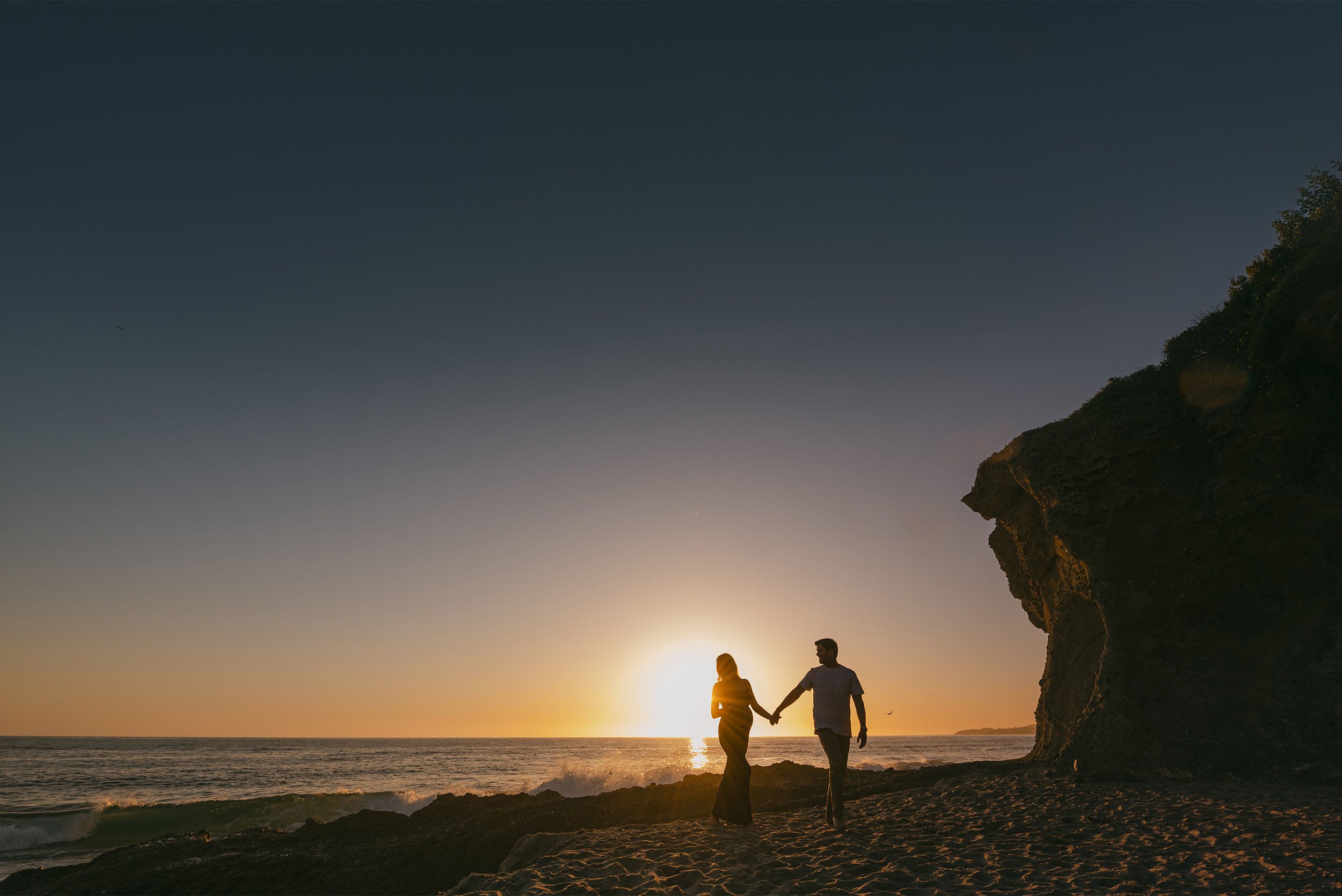 Silhouette of couple holding hands on beach at sunset, highly recommended maternity photographer Orange County