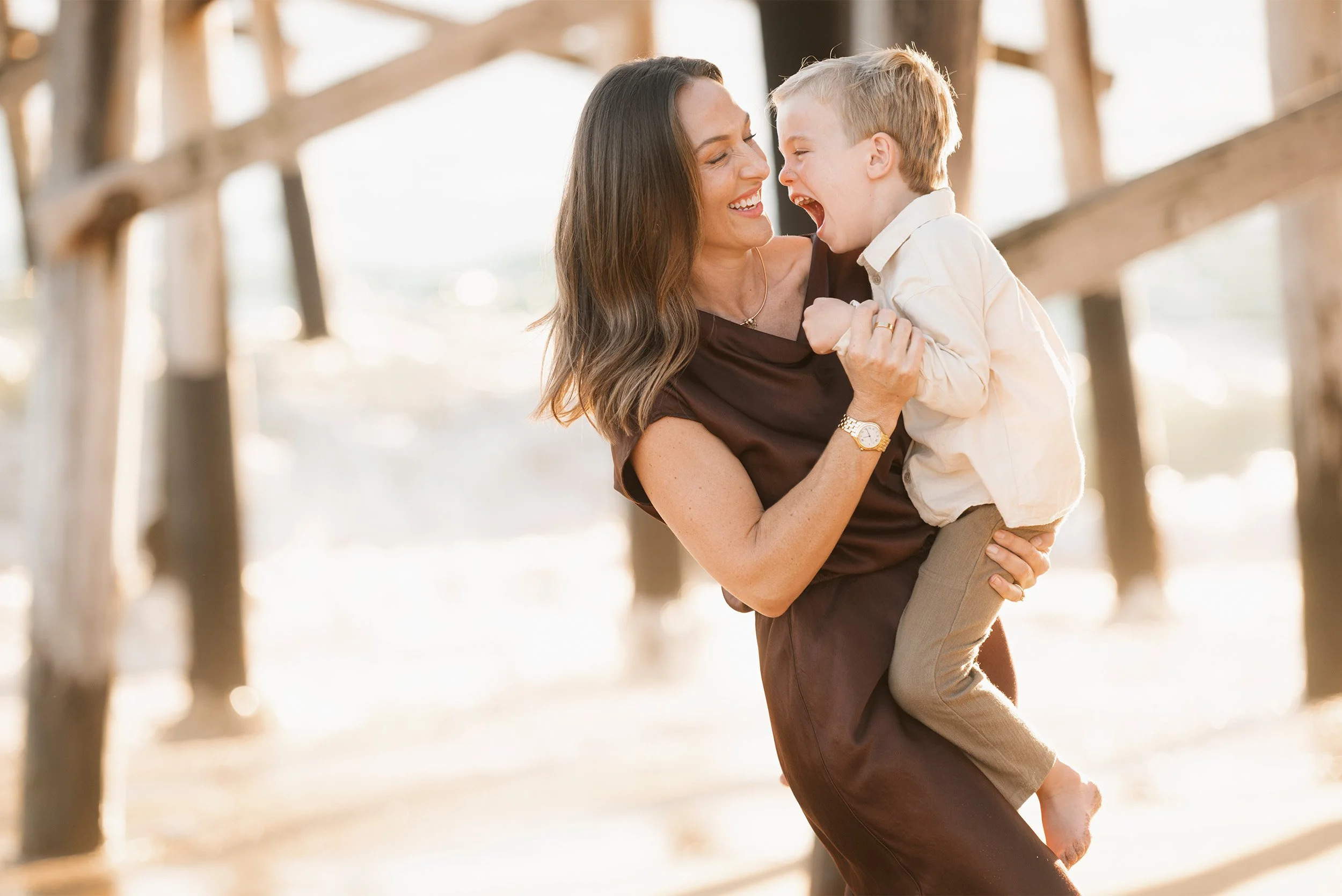 Award-winning family photographer in Orange County captures joyful mother-son moment under beach pier