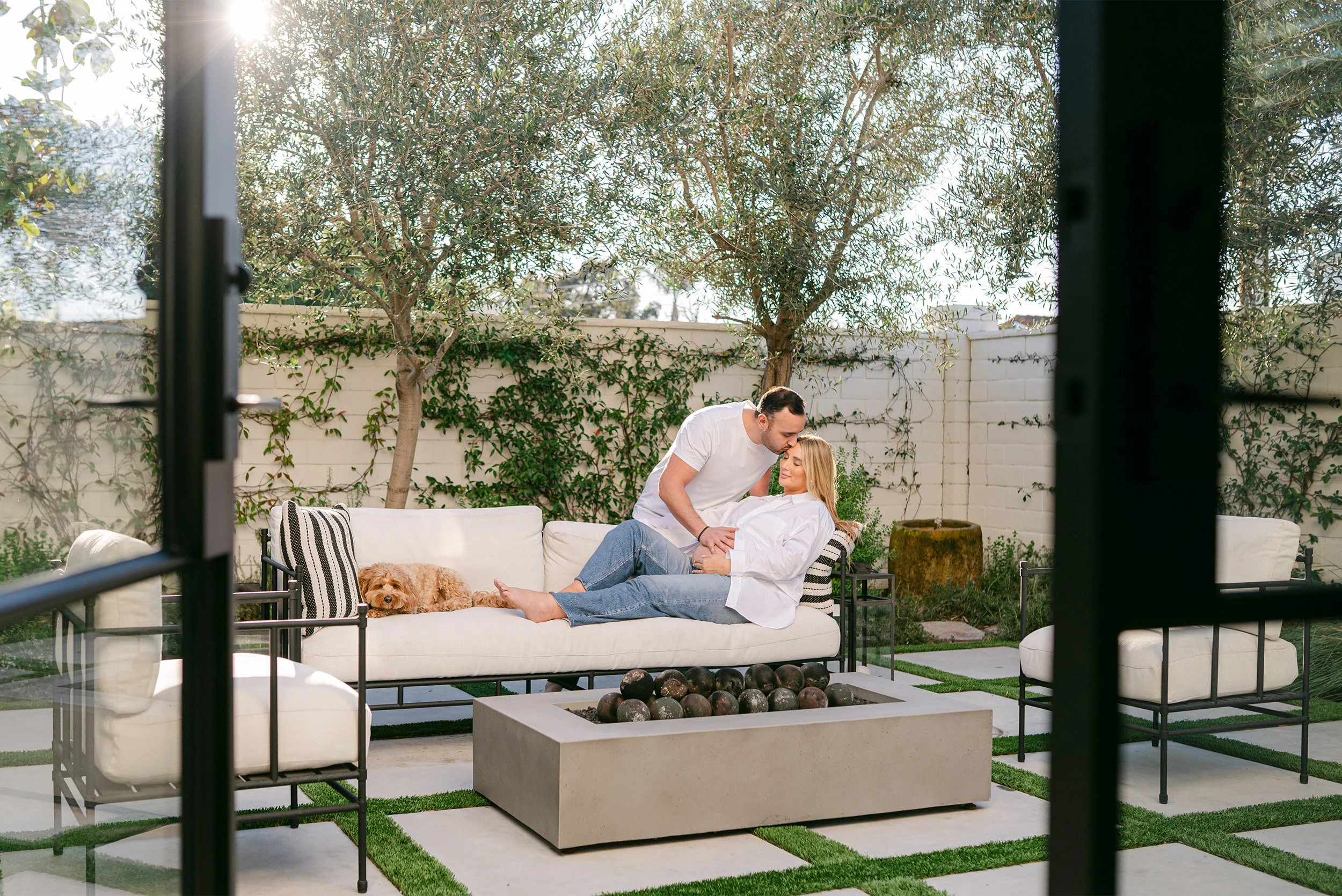 Couple embracing on outdoor sofa with dog in backyard, pet-friendly and award-winning maternity photographer in Orange County