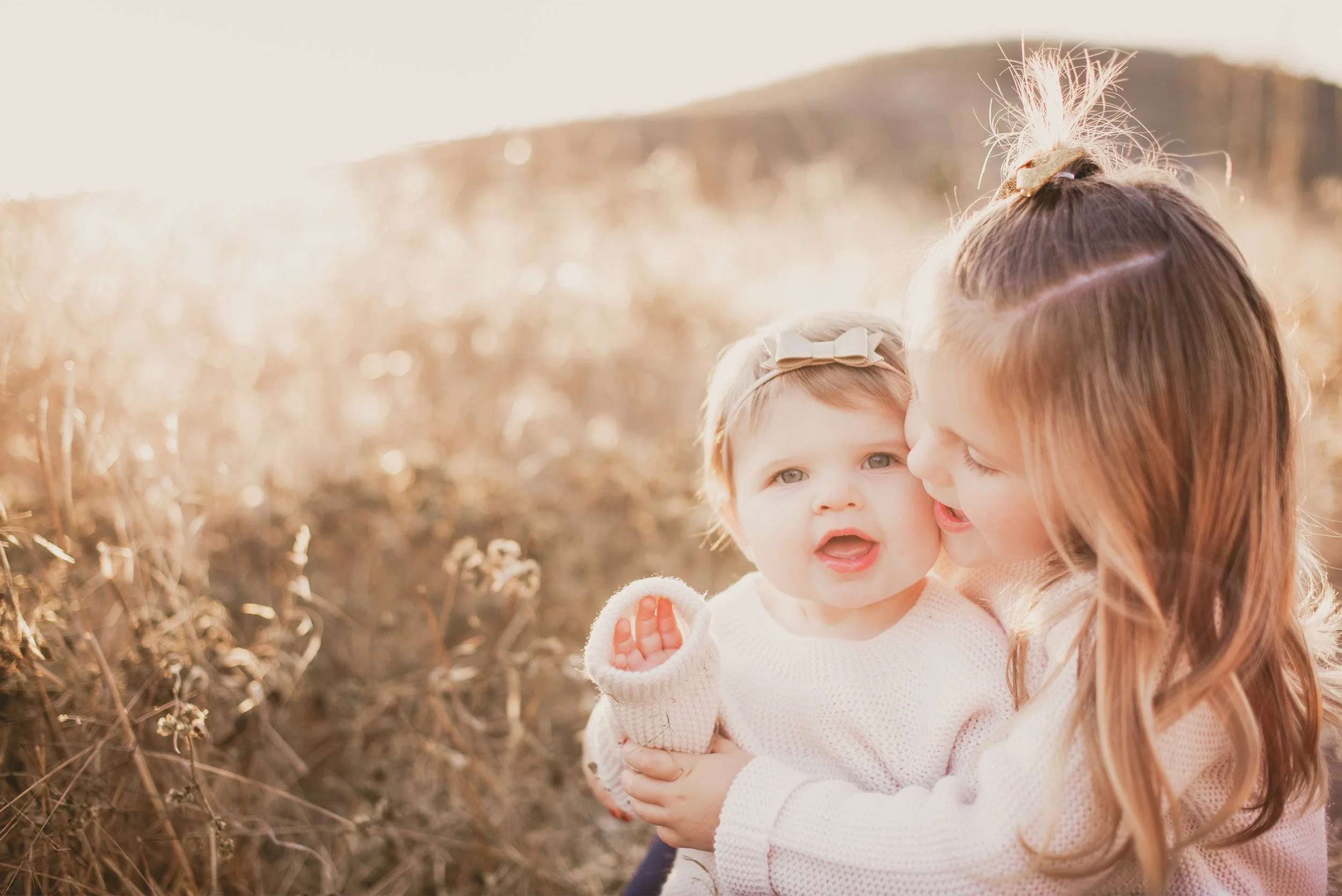 Orange County family photographer captures tender sibling moment between two sisters in golden field light