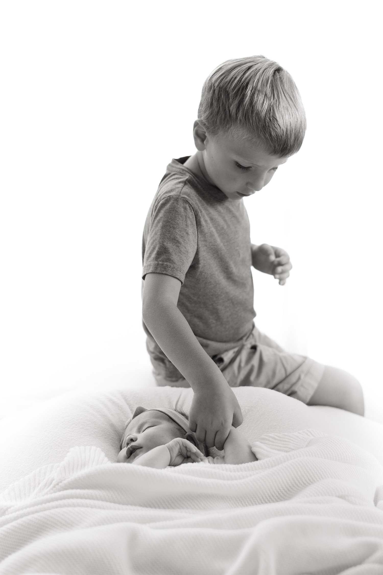 Black and white photo of big brother gently touching sleeping newborn, award-winning baby photographer in Orange County