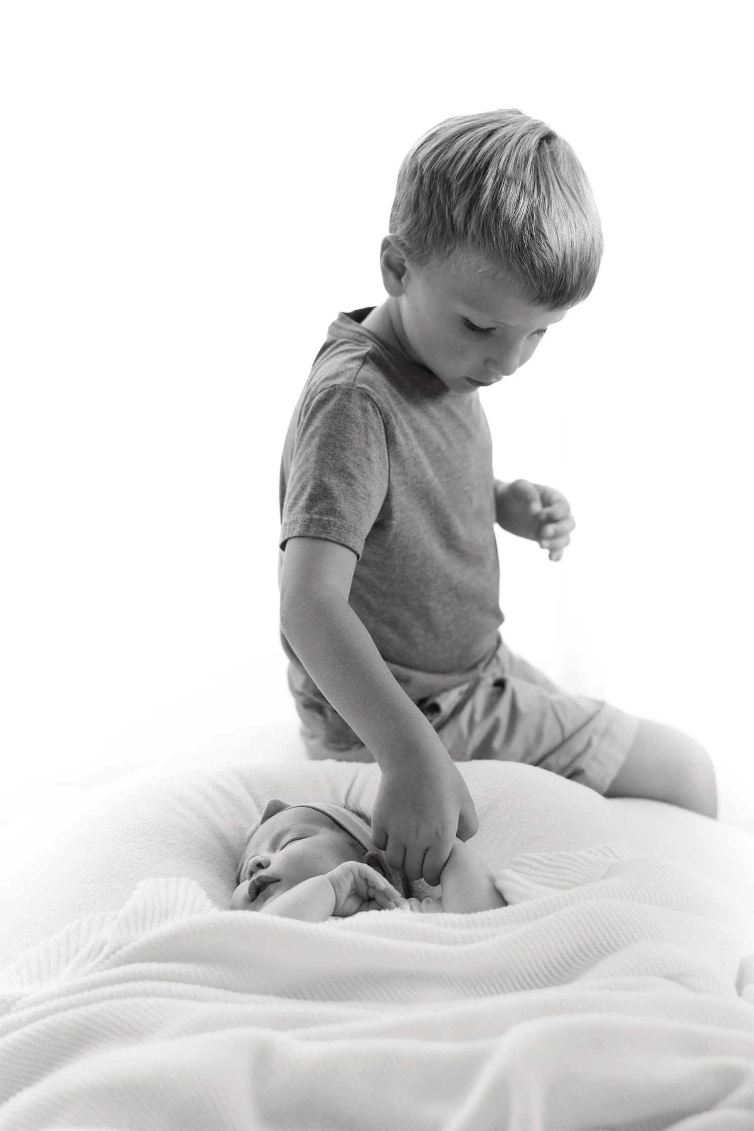 Black and white photo of big brother gently touching sleeping newborn, award-winning baby photographer in Orange County, in home newborn baby photos