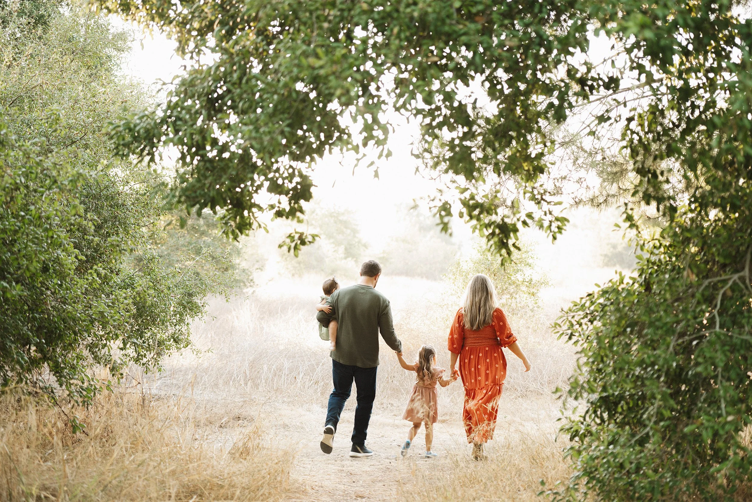 Orange County family photography featuring family of four walking hand-in-hand through sunlit meadow