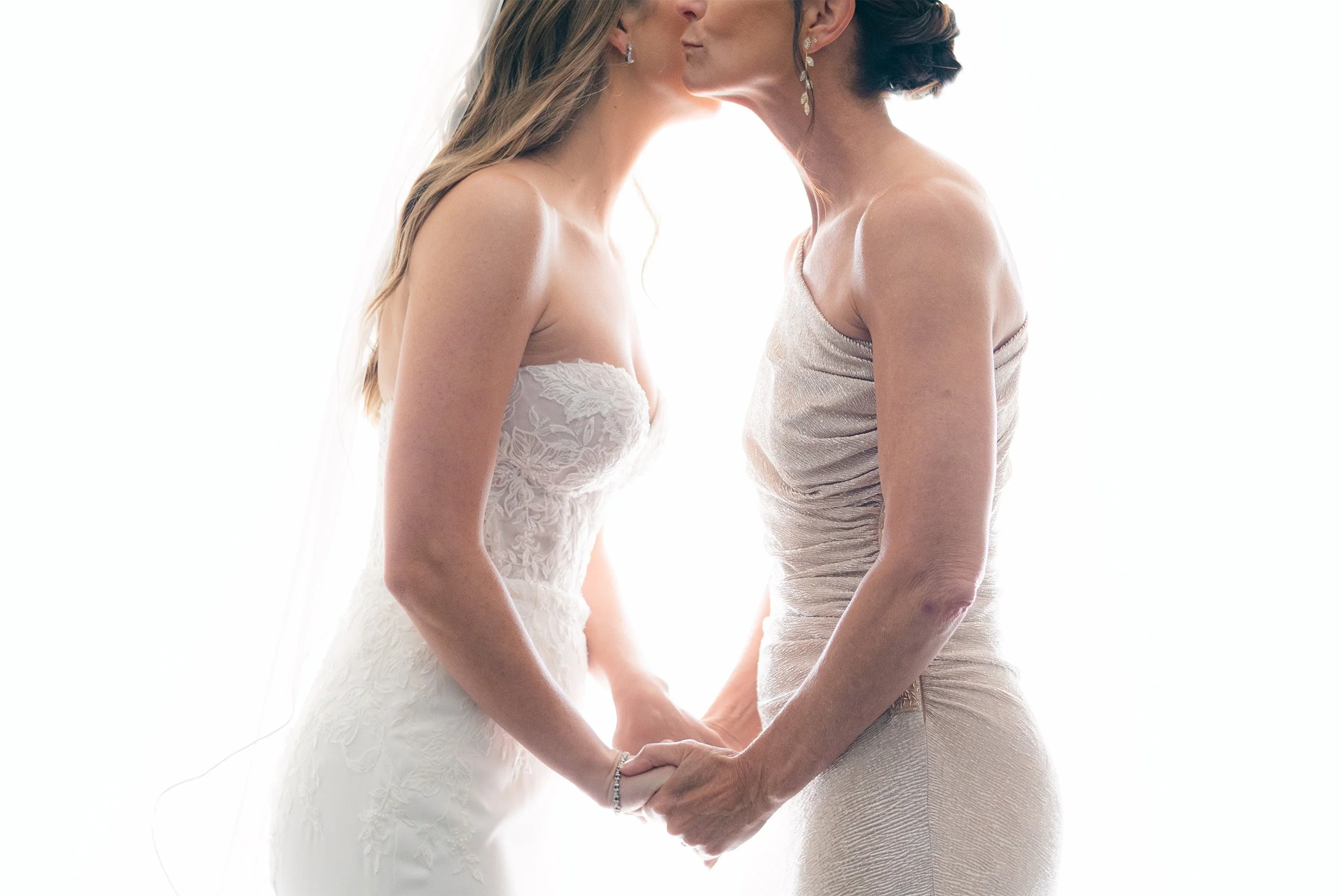 Orange County wedding photographer captures tender backlit moment between bride and mother holding hands before ceremony at the Gardener Ranch in Carmel Valley