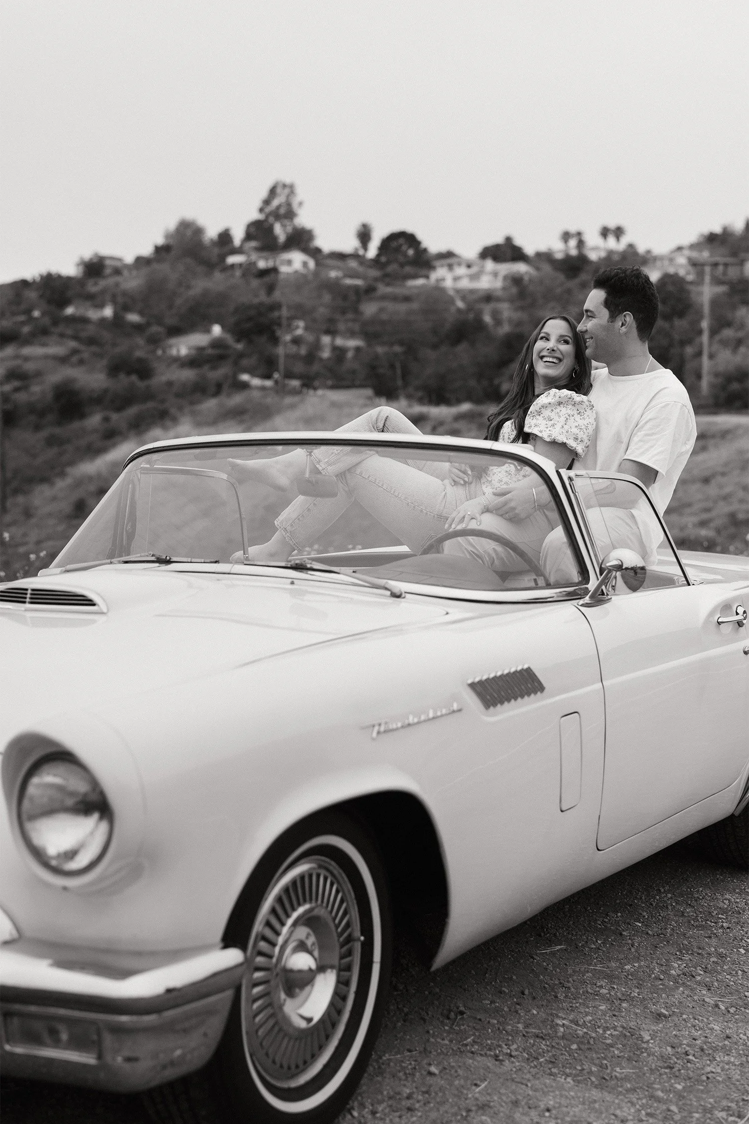 Award-winning engagement photographer in Malibu captures couple laughing in vintage convertible on hillside road