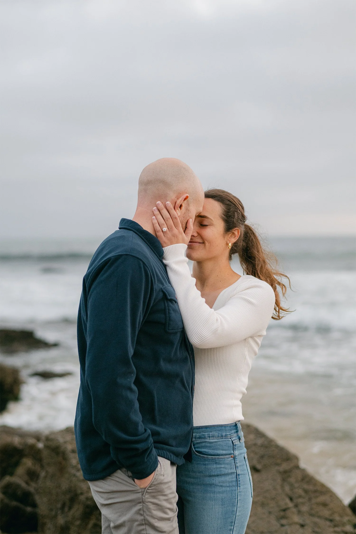 Orange County engagement photographer captures tender embrace in Crystal Cove under moody coastal sky