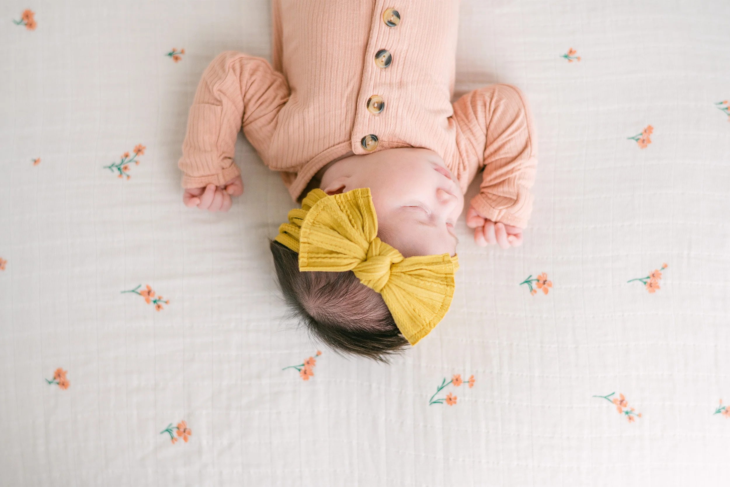 Overhead view of sleeping newborn in peach outfit with yellow bow, Orange County baby photographer