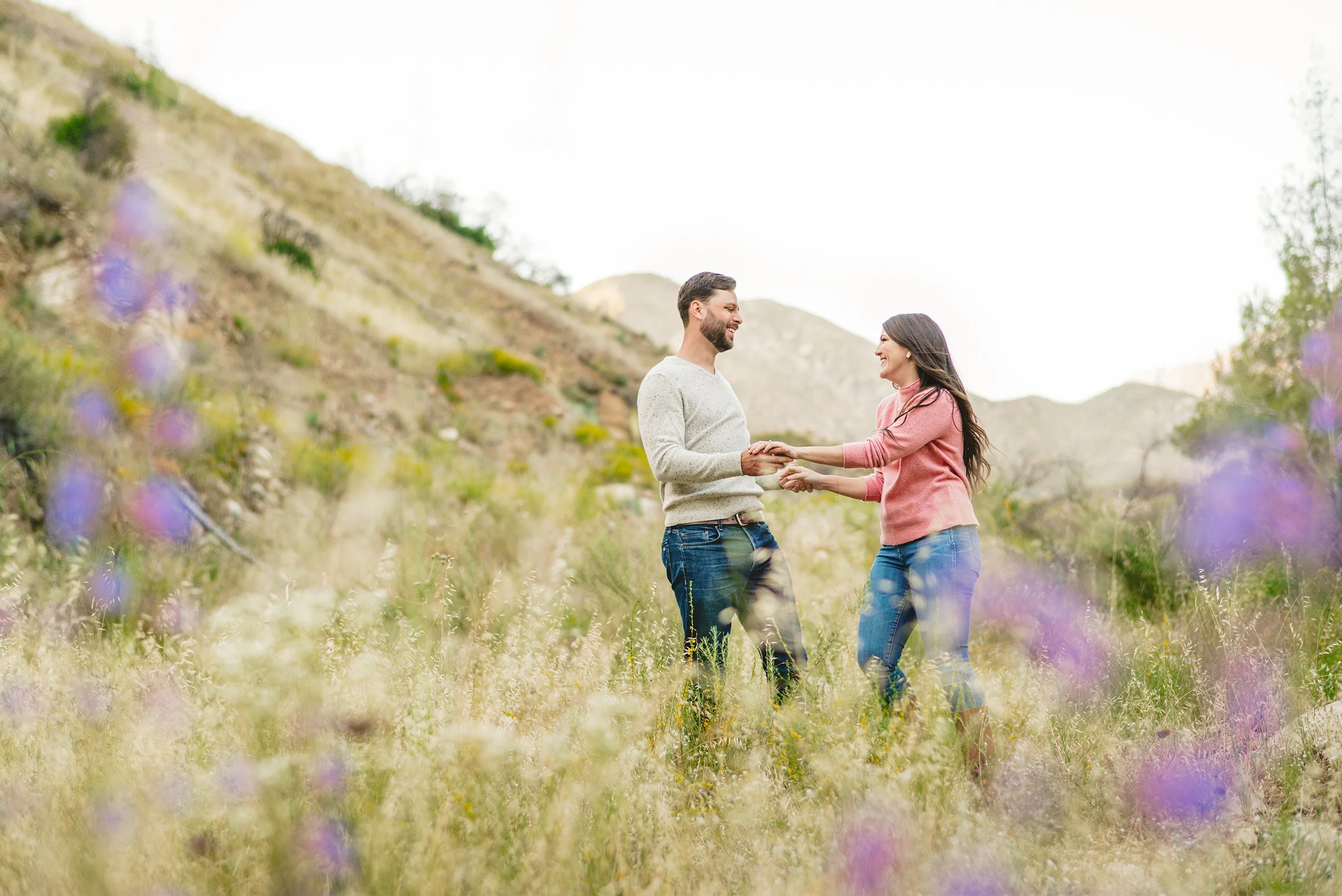 Couple laughing and holding hands in wildflower field, Orange County engagement photographer