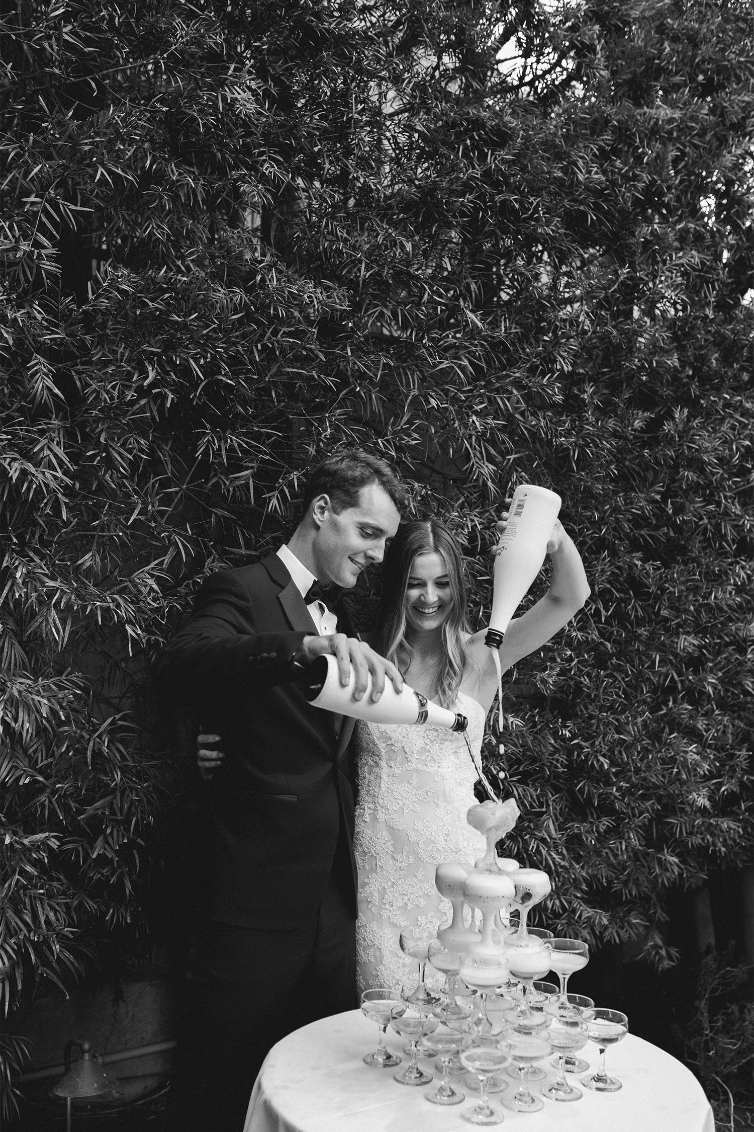Bride and groom pouring champagne tower together, black and white reception celebration photo