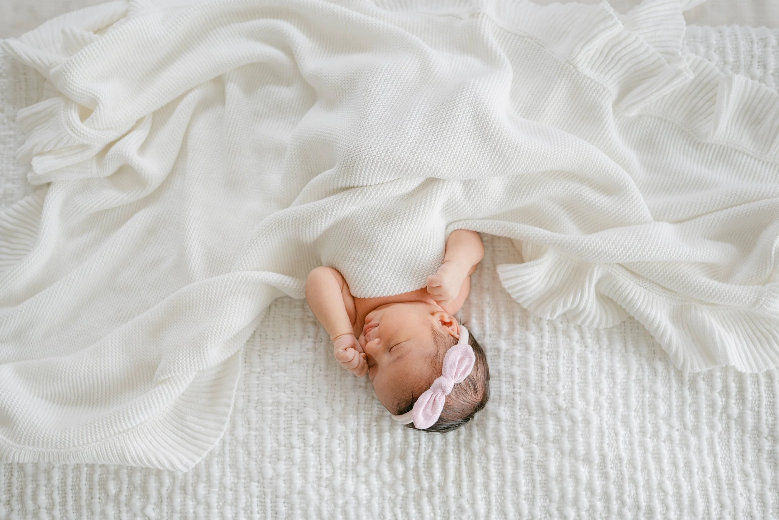 Newborn peeking out from under white knit blanket with pink bow headband, highly recommended baby photographer in Orange county