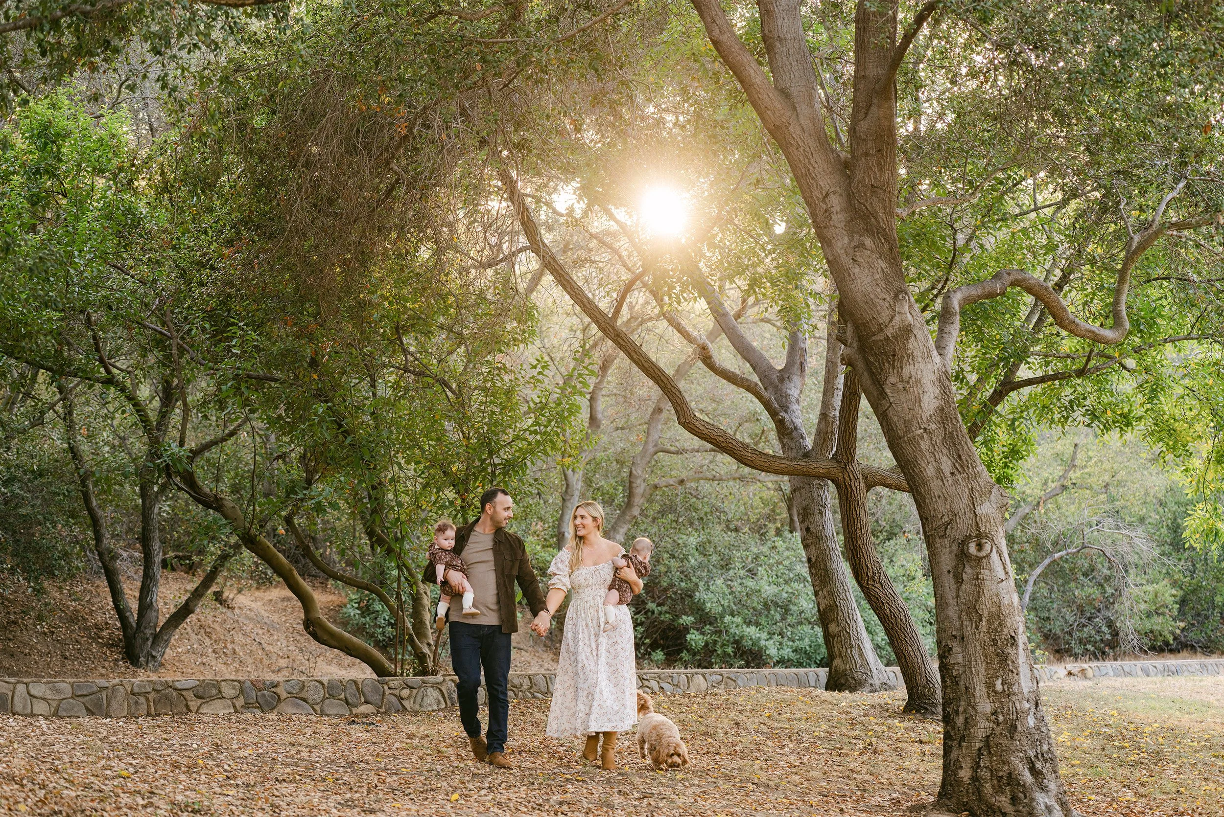 Pet-friendly Orange County family photographer captures family walk with twins and dog among the trees in Irvine Park