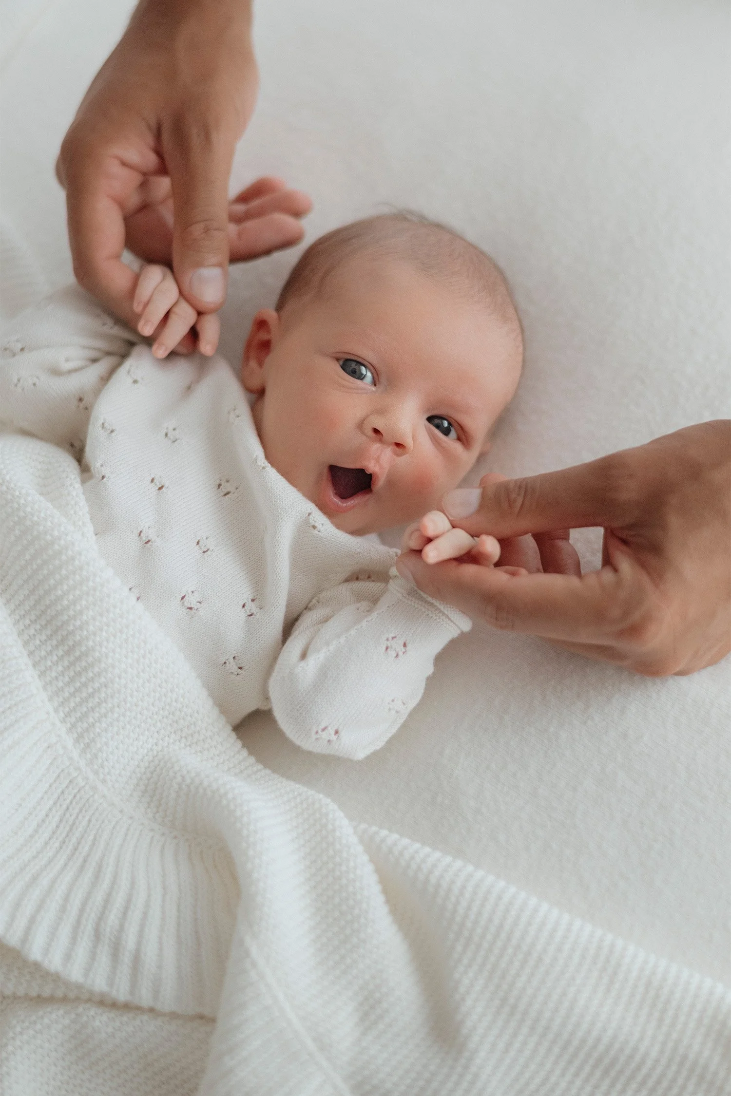 Award-winning newborn photographer in Orange County captures baby's yawn while parents hold tiny fingers, in home newborn photos