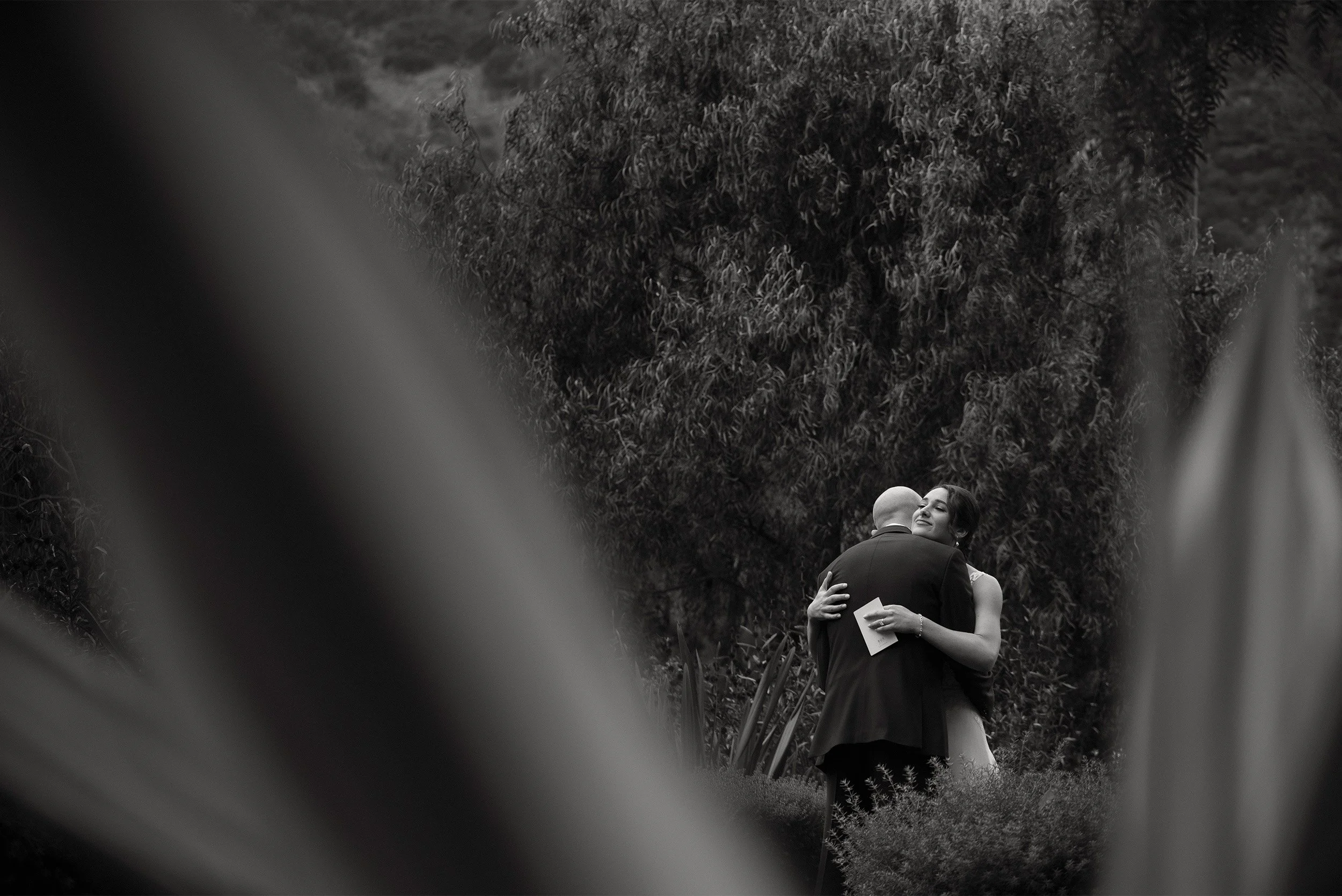 Orange County wedding photographer captures intimate embrace between bride and groom framed by palm fronds, black and white taken at The Ranch at Laguna Beach
