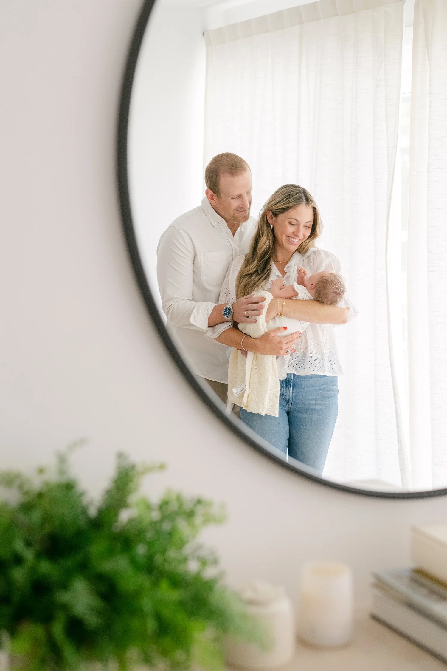 Parents holding newborn reflected in round mirror by window, highly recommended baby photographer Orange County