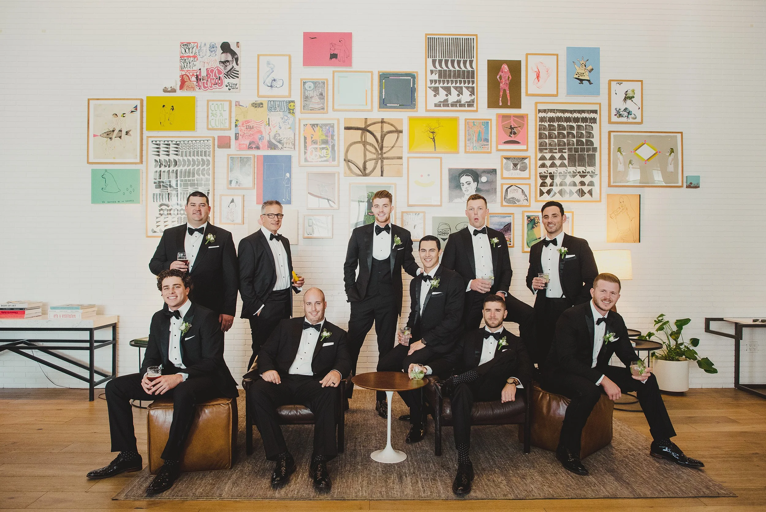 Groomsmen in black tuxedos posing in front of colorful gallery art wall, Orange County wedding photography