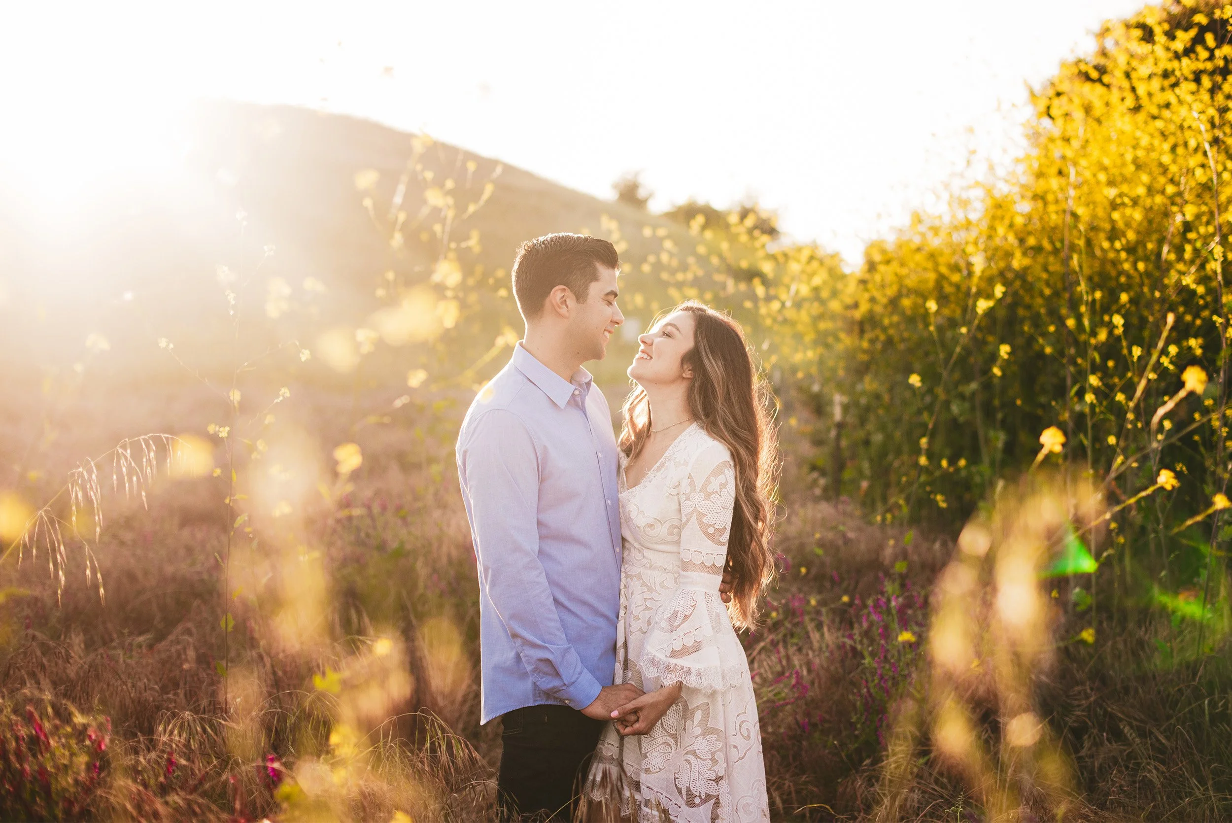 Bride and groom laughing together in a golden wildflower field at sunset, romantic engagement photography
